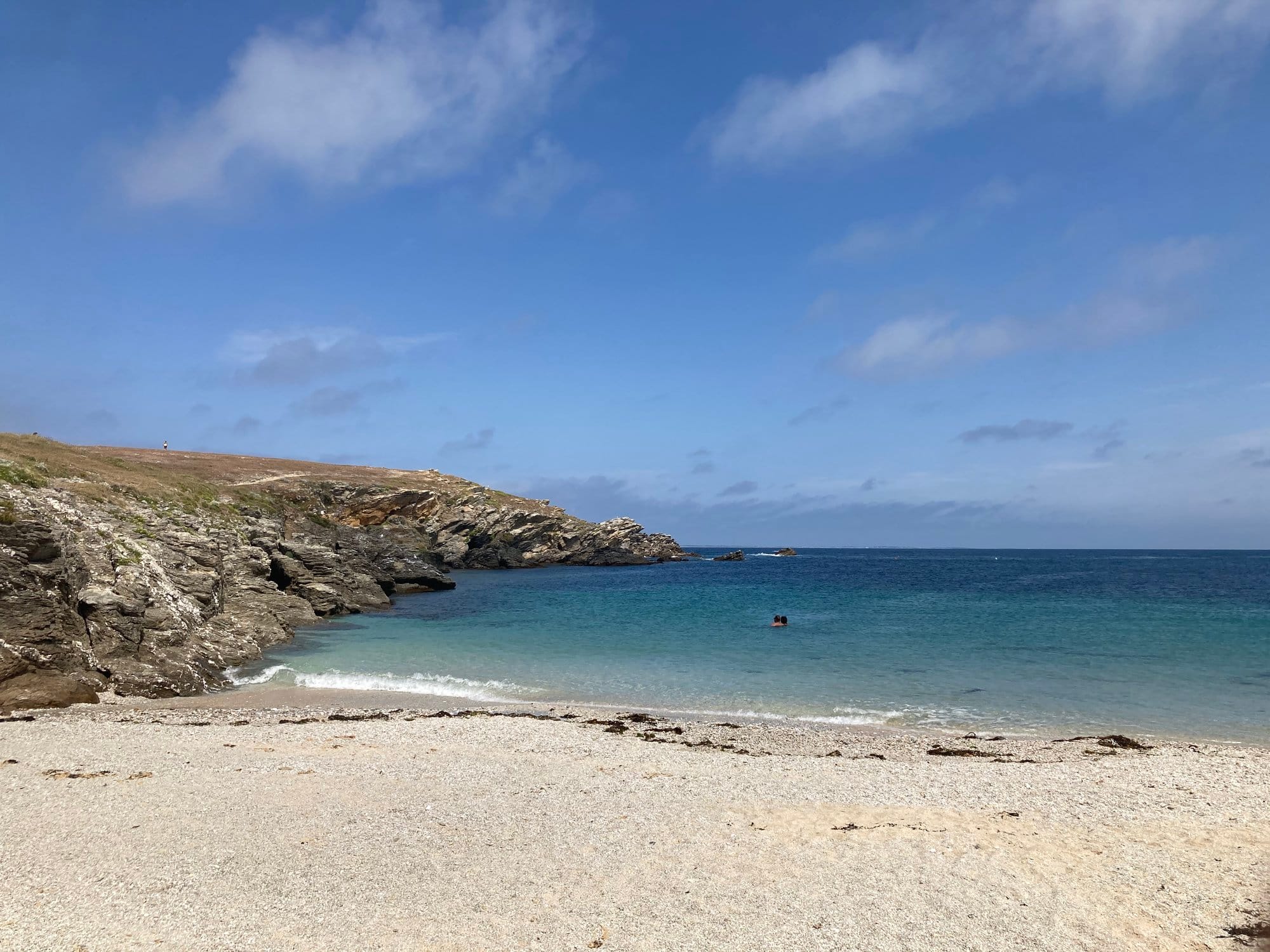 A quiet sandy cove near Pointe des Poulains, bright turquoise water, rocky headland curving around the bay, almost empty beach