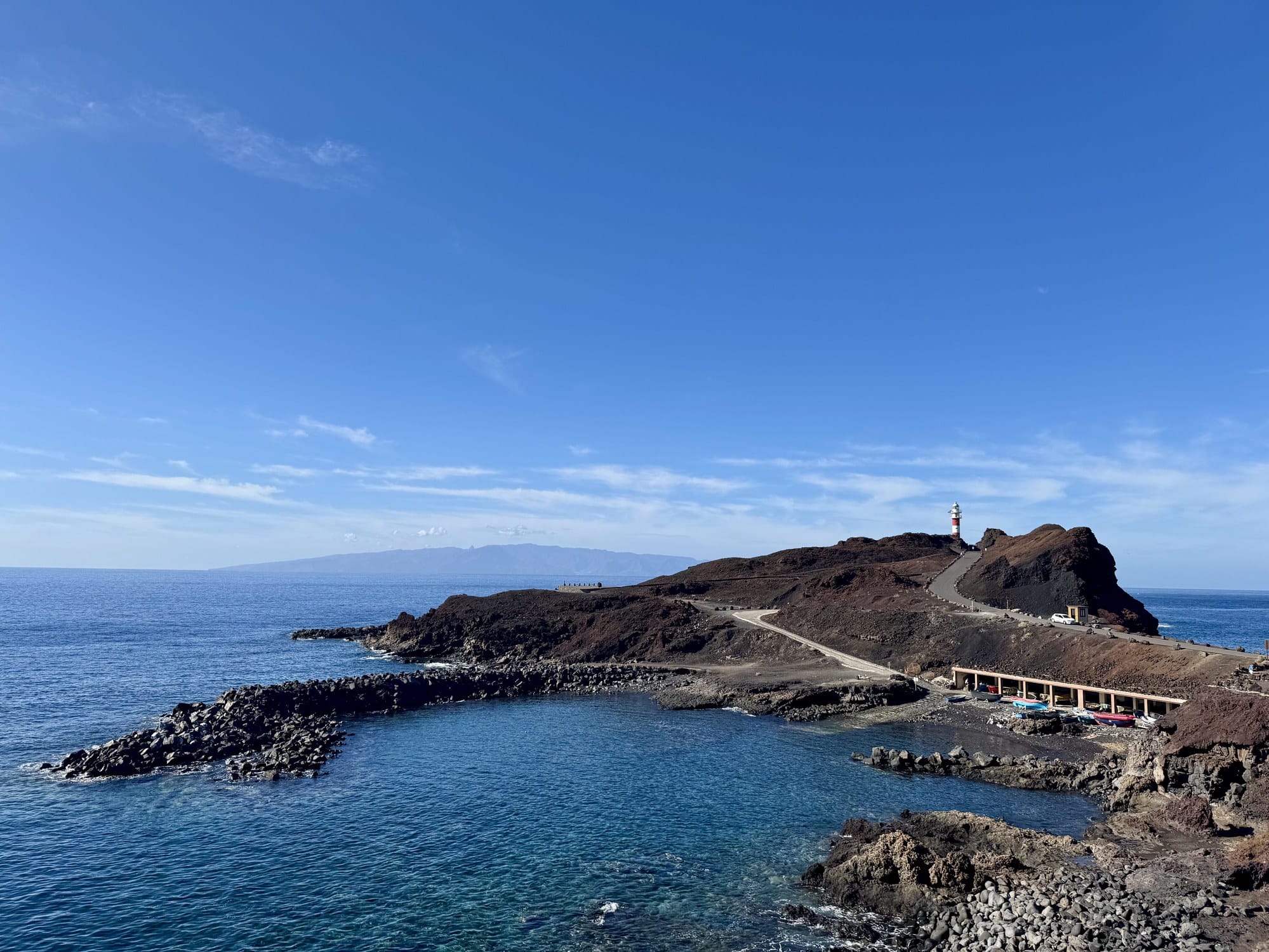 The red-and-white striped Punta de Teno lighthouse with natural seawater pool and La Gomera on the horizon — Tenerife