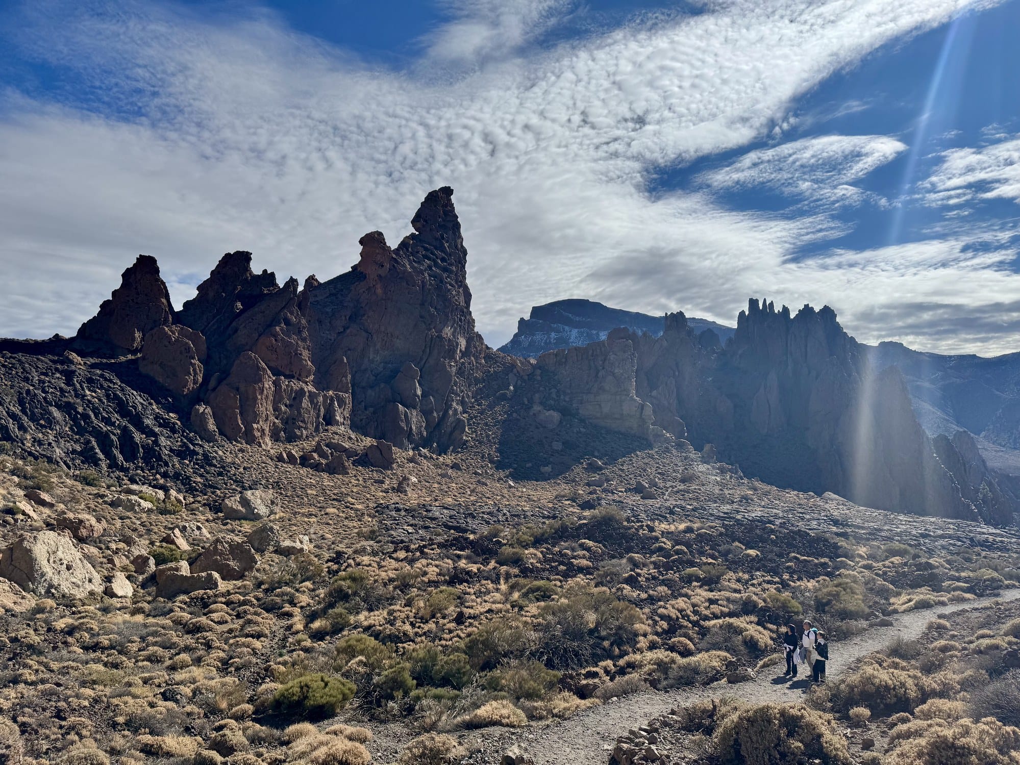 Hikers on the Roques de García trail with towering volcanic rock pillars and the caldera wall in the background — Teide National Park, Tenerife