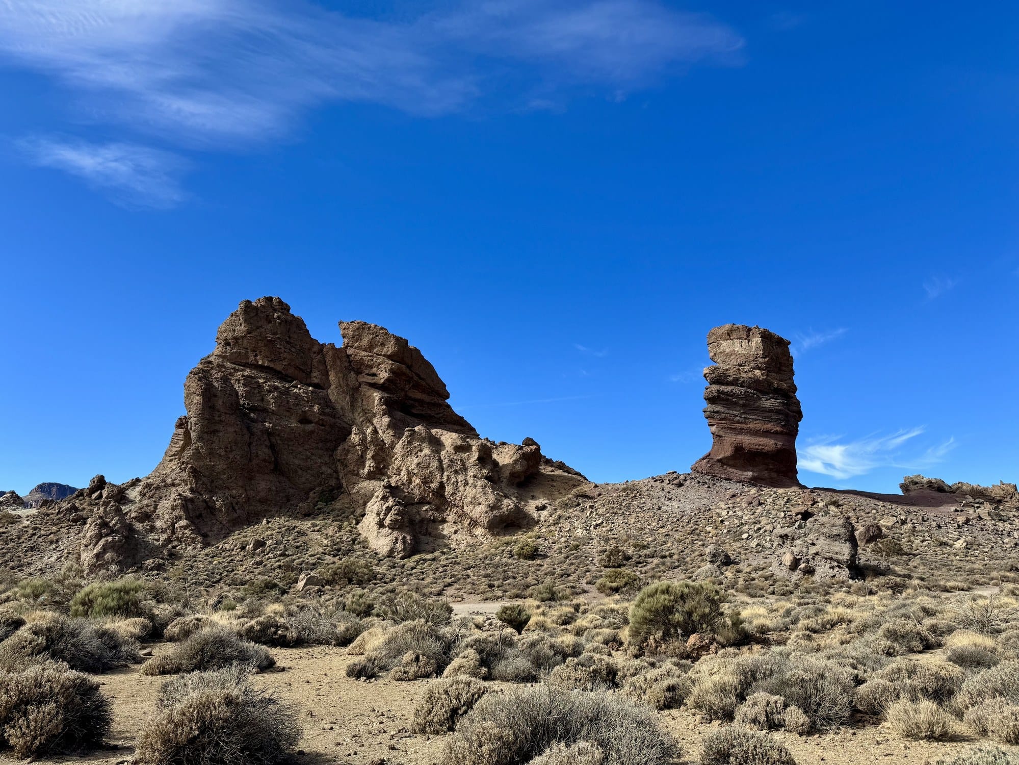 Two massive rock pillars of the Roques de García under a blue sky, with dry vegetation in the foreground — Teide National Park, Tenerife