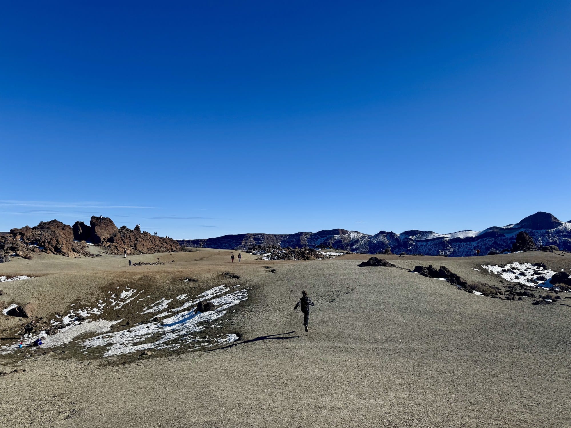 A wide sandy volcanic landscape with rock formations and a small running figure — Minas de San José, Teide National Park, Tenerife