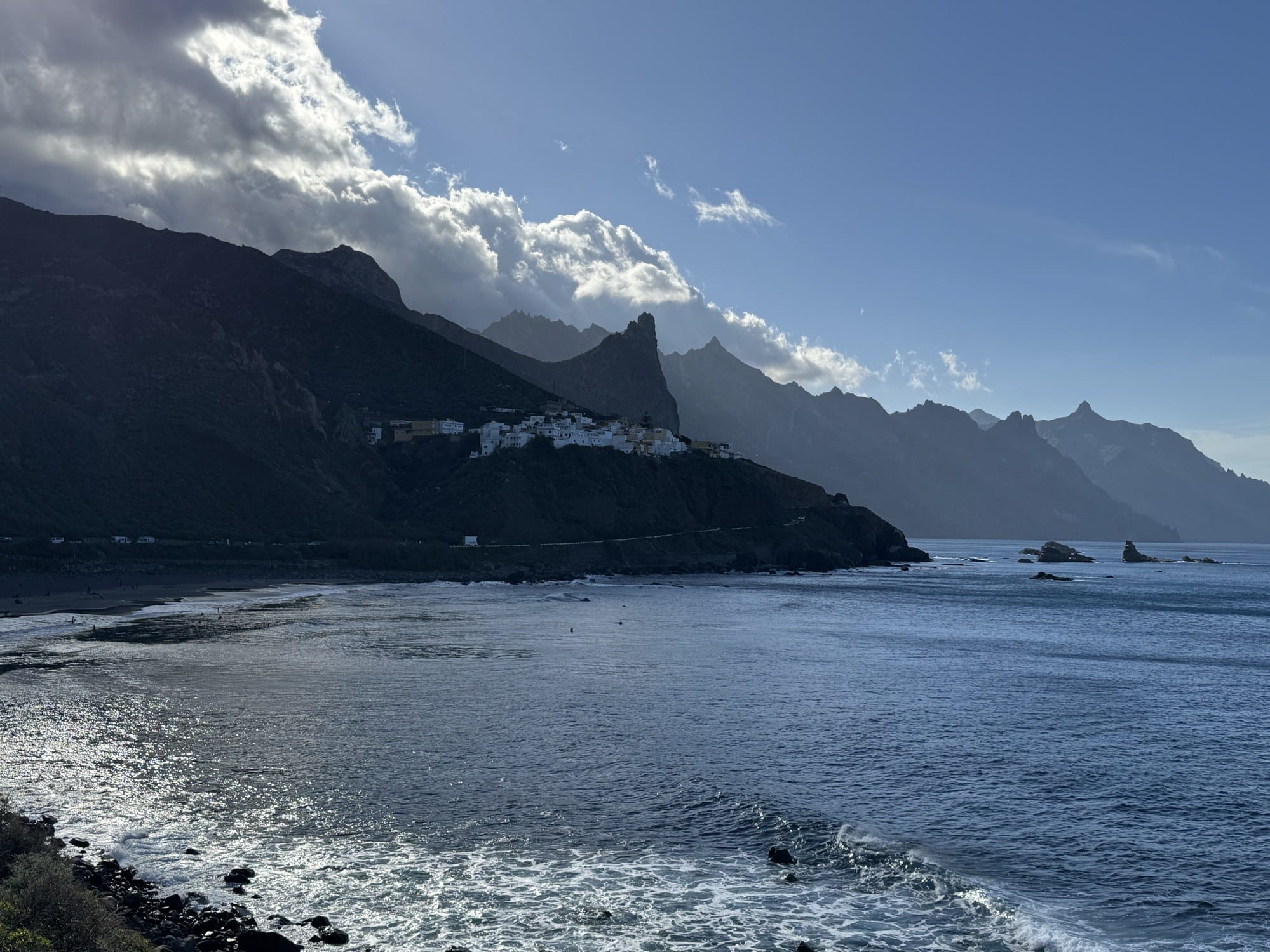 The rocky Atlantic coast of Anaga near Almáciga, with pointed sea stacks rising from the water and a black-sand beach in the foreground — Tenerife