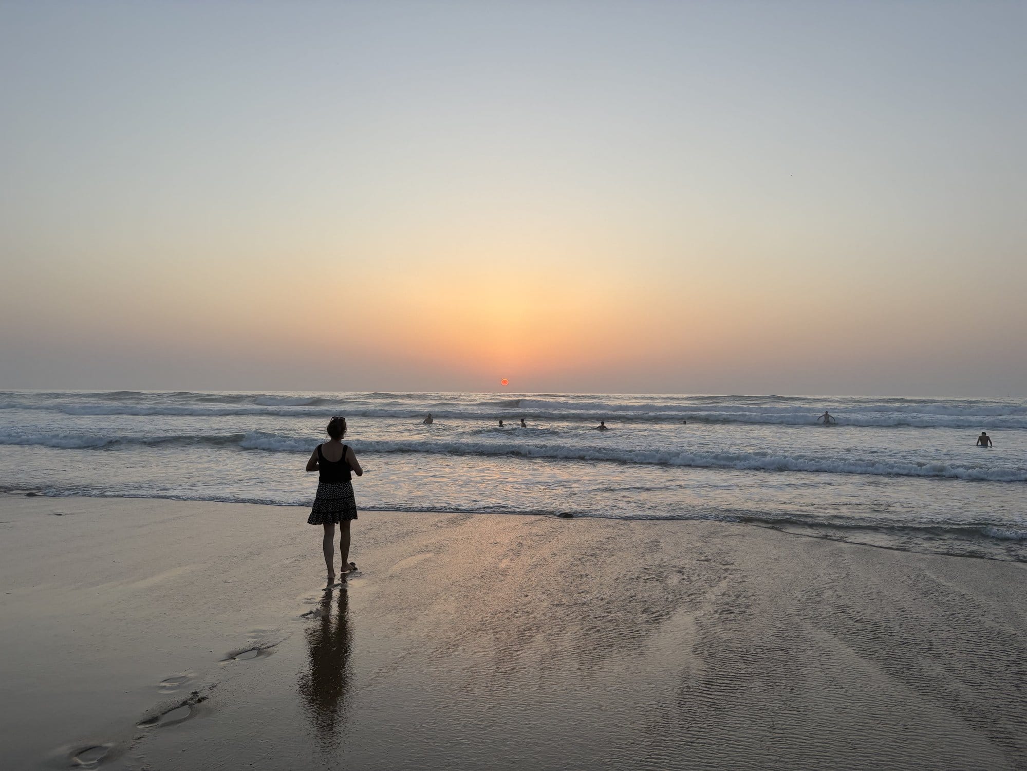 Sunset on Bidart beach with a silhouette walking towards the waves, surfers in the water and golden reflections on the wet sand — French Basque Country