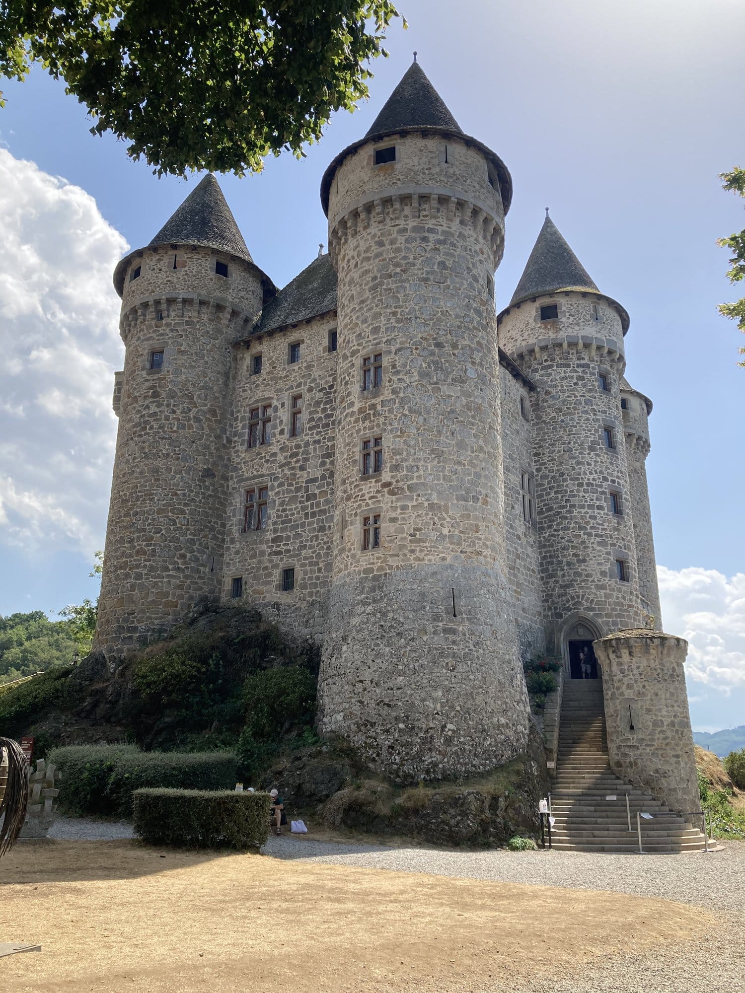 The medieval Château de Val with its stone towers and conical slate roofs, seen from the entrance courtyard — Lanobre, Auvergne, France