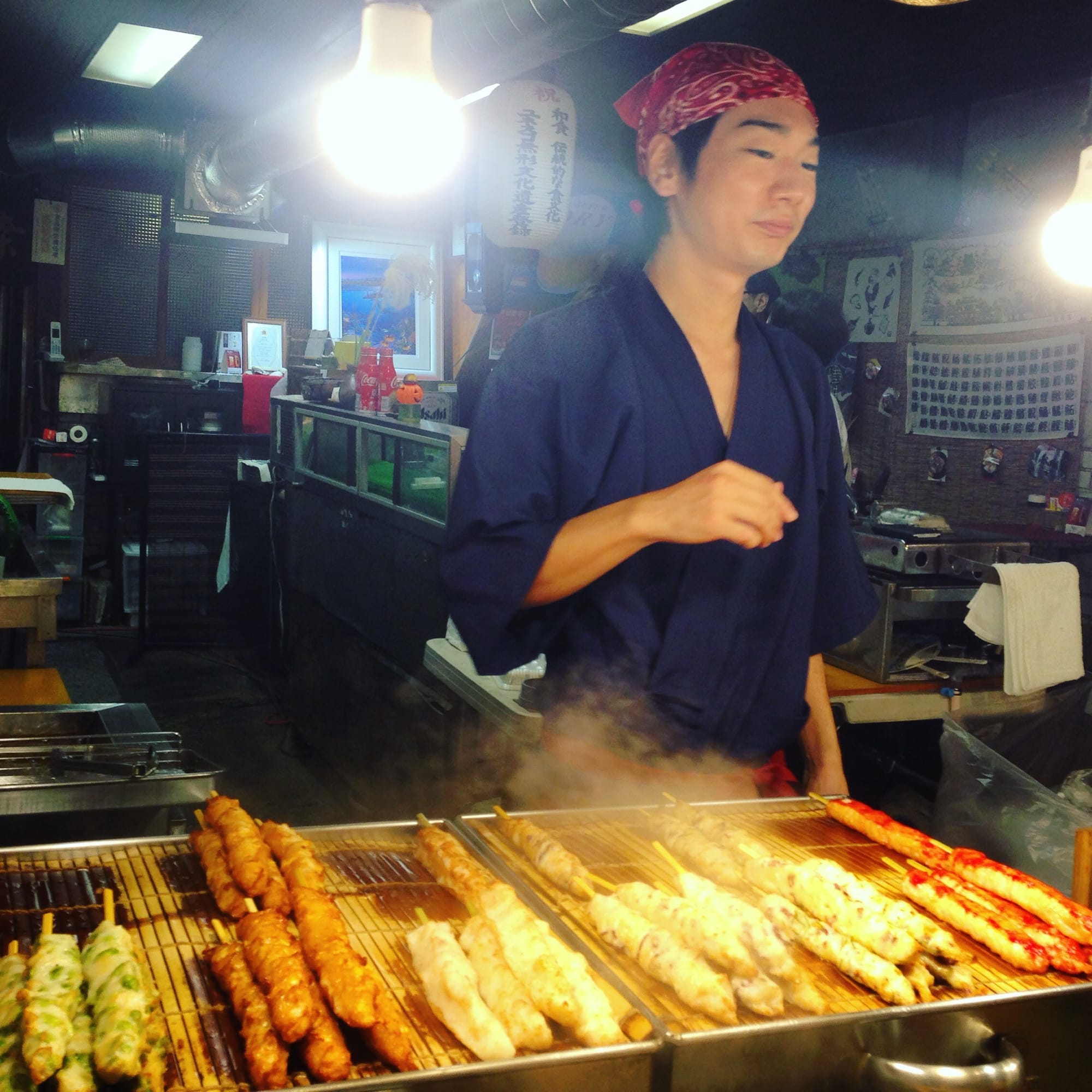 A yakitori vendor grills skewers under hanging lanterns in a Kyoto arcade — Nishiki Market area, Kyoto, Japan