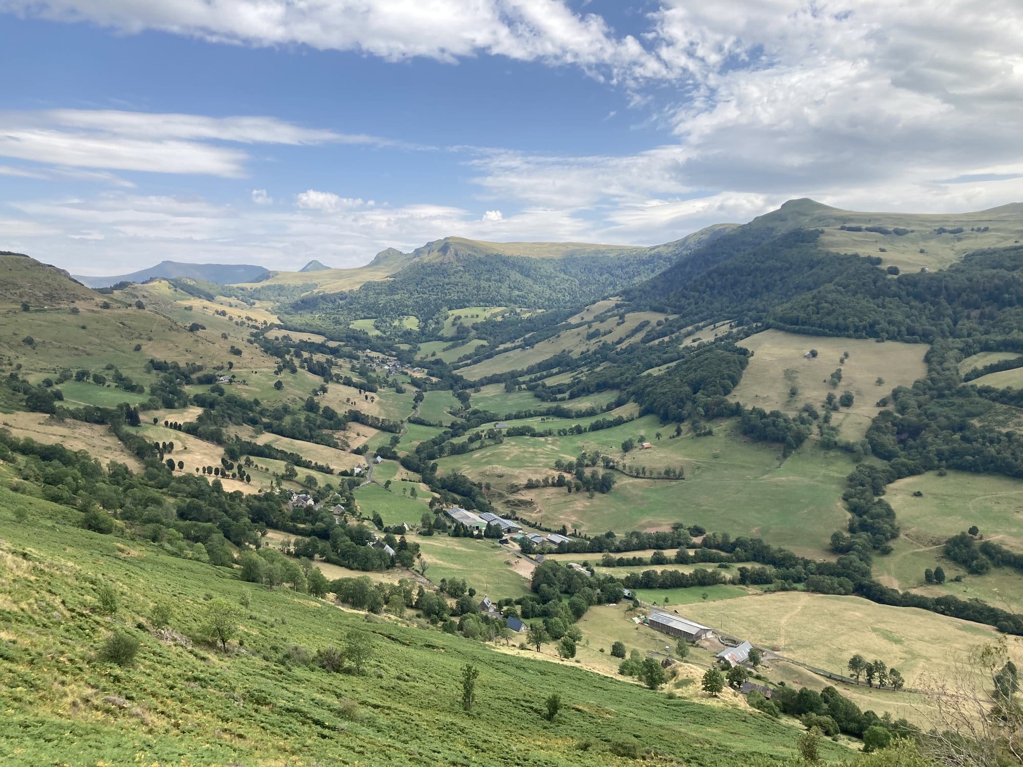 Sweeping panoramic view of the Vallée du Falgoux from the volcanic ridge, with green pastures and hamlets in the valley below — Cantal, Auvergne, France