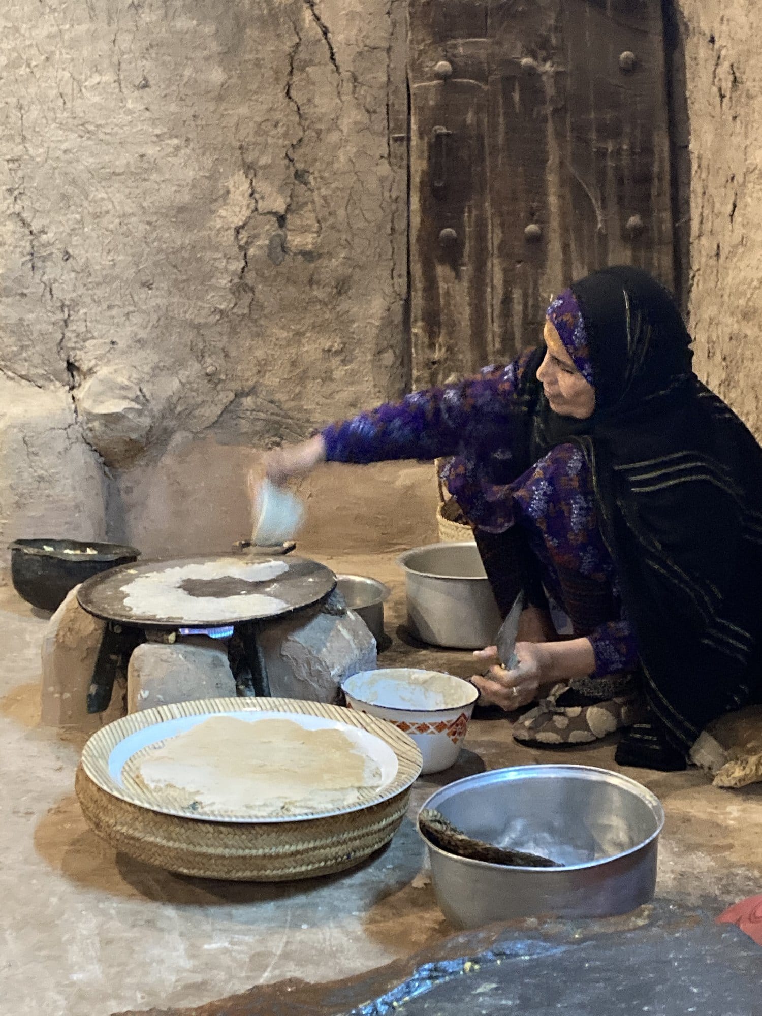 Omani woman in traditional dress making bread on a stone oven in a traditional house — Bahlā', Oman
