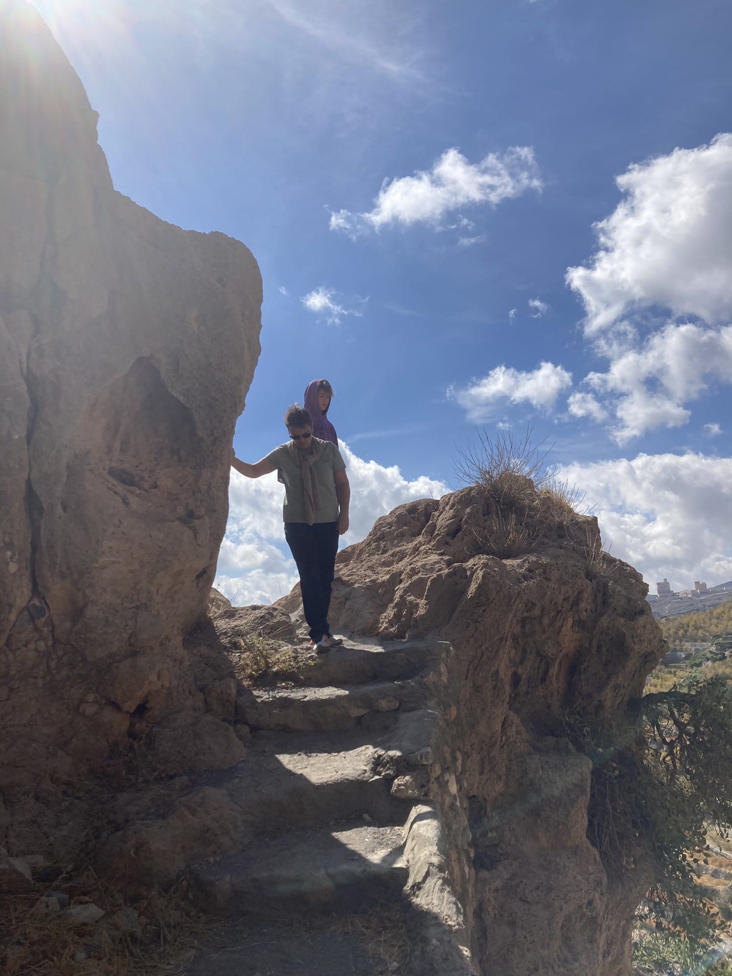 Figure sitting at the edge of a deep canyon, contemplating the vast mountain valley below — Jebel Akhdar, Oman
