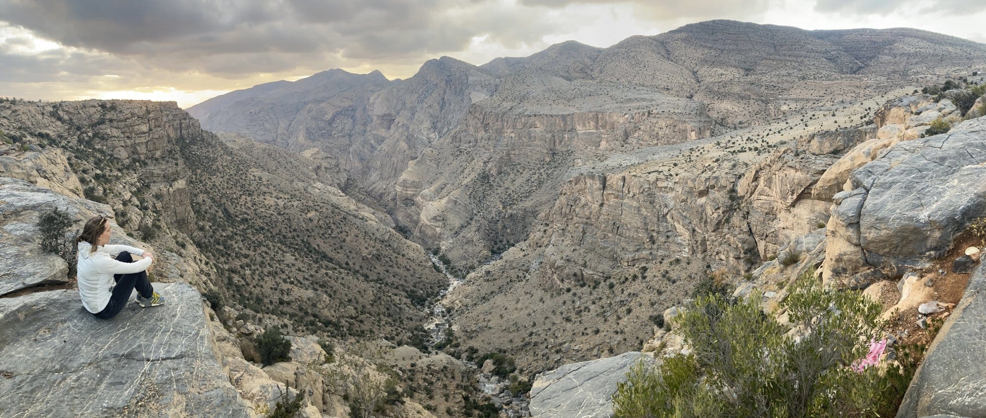 Person sitting on the edge of a massive canyon at sunset, silhouetted against the sky at 1,900m — Jebel Akhdar, Oman