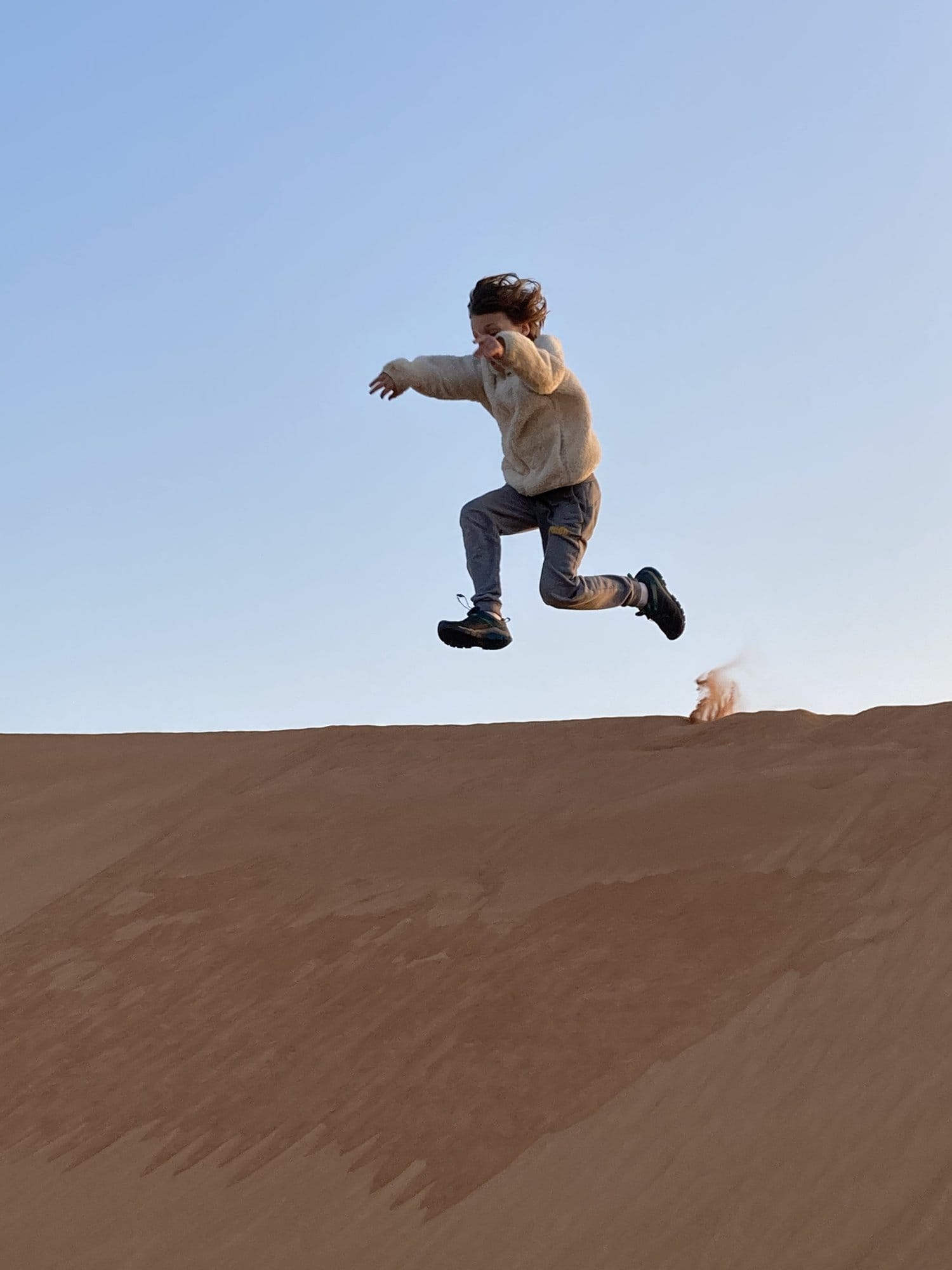 Child leaping mid-air above a sand dune ridge in the clear morning light โ Wahiba Sands, Oman