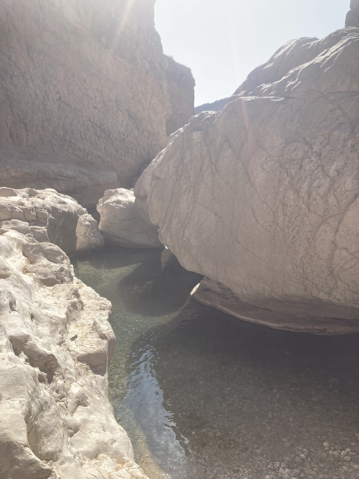 Narrow passage between giant polished boulders with emerald water below — Wadi Bani Khalid, Oman
