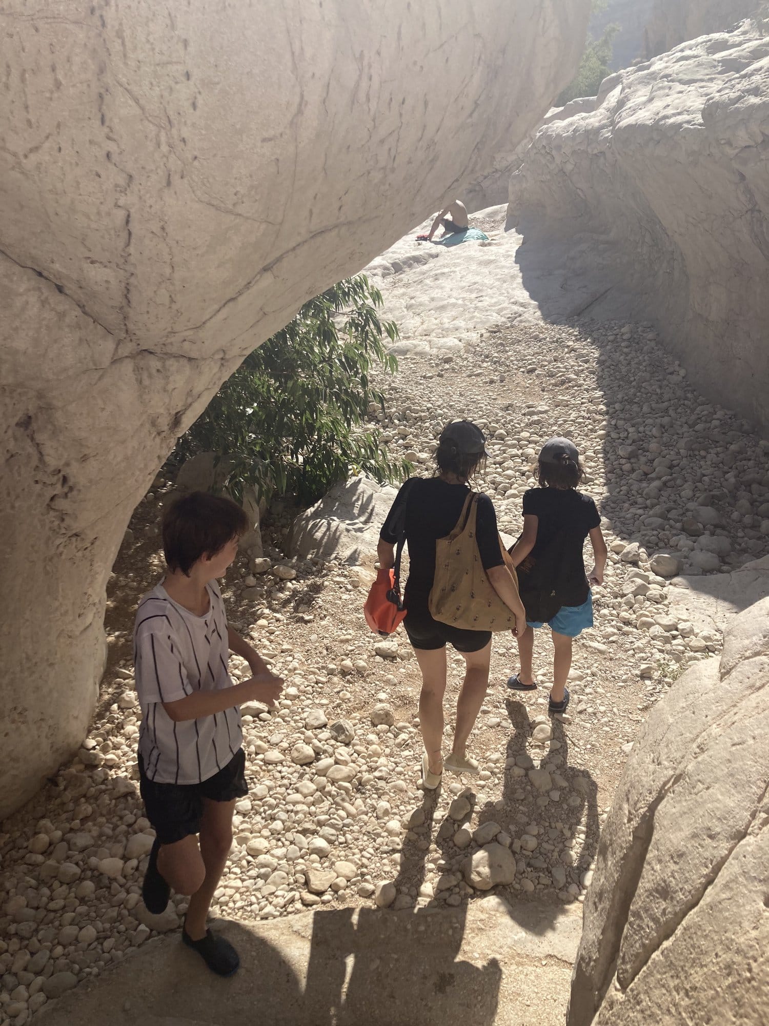Family walking through a rock arch in the wadi, seen from behind — Wadi Bani Khalid, Oman