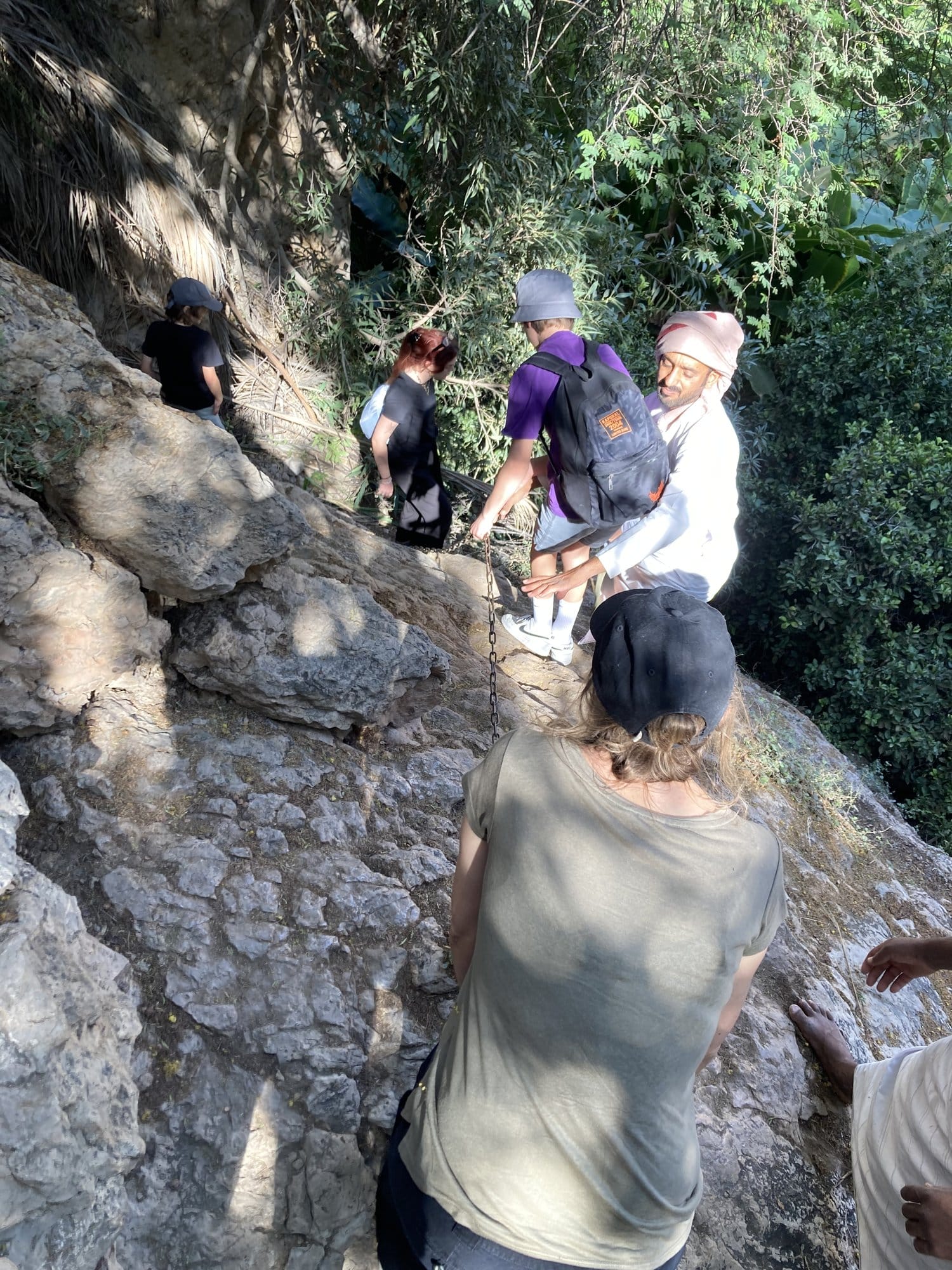 Group descending a rock face using a chain, with tropical vegetation around — Wadi Tiwi, Oman