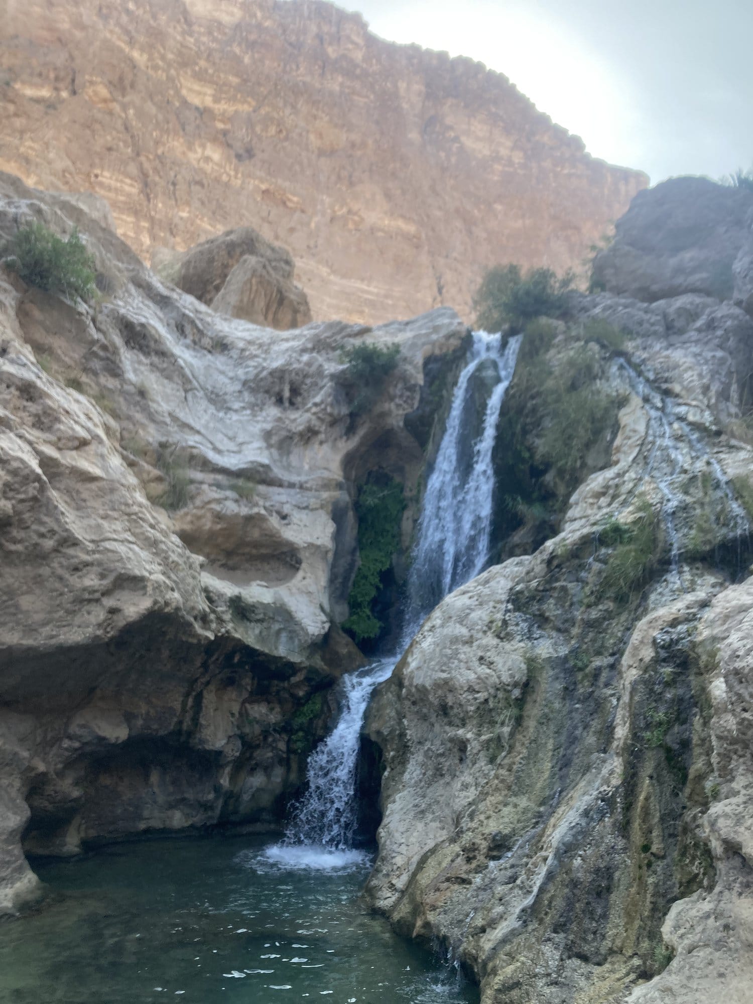 A waterfall cascading into a rock pool deep inside Wadi Tiwi — Sur, Oman