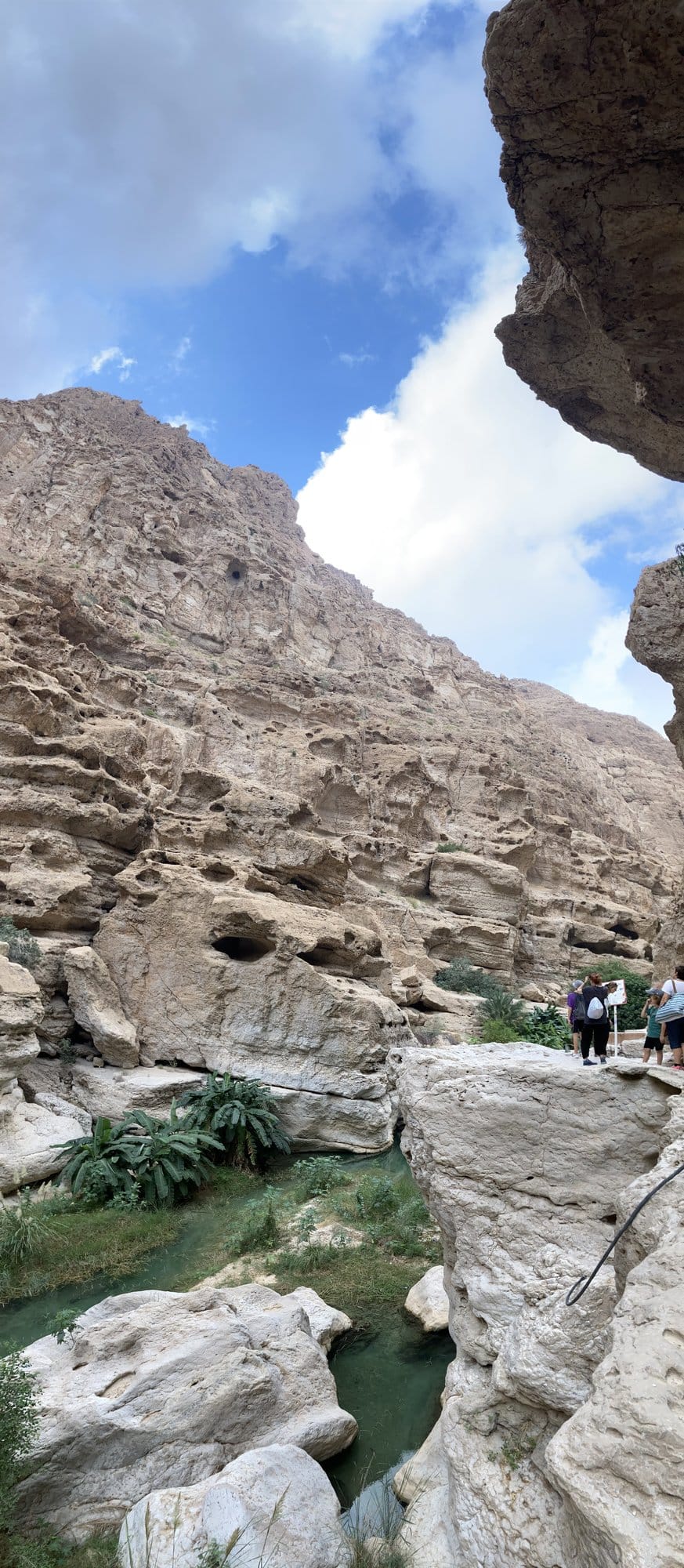 The towering canyon of Wadi Shab with an emerald pool and distant hikers on the rocks — Sur, Oman