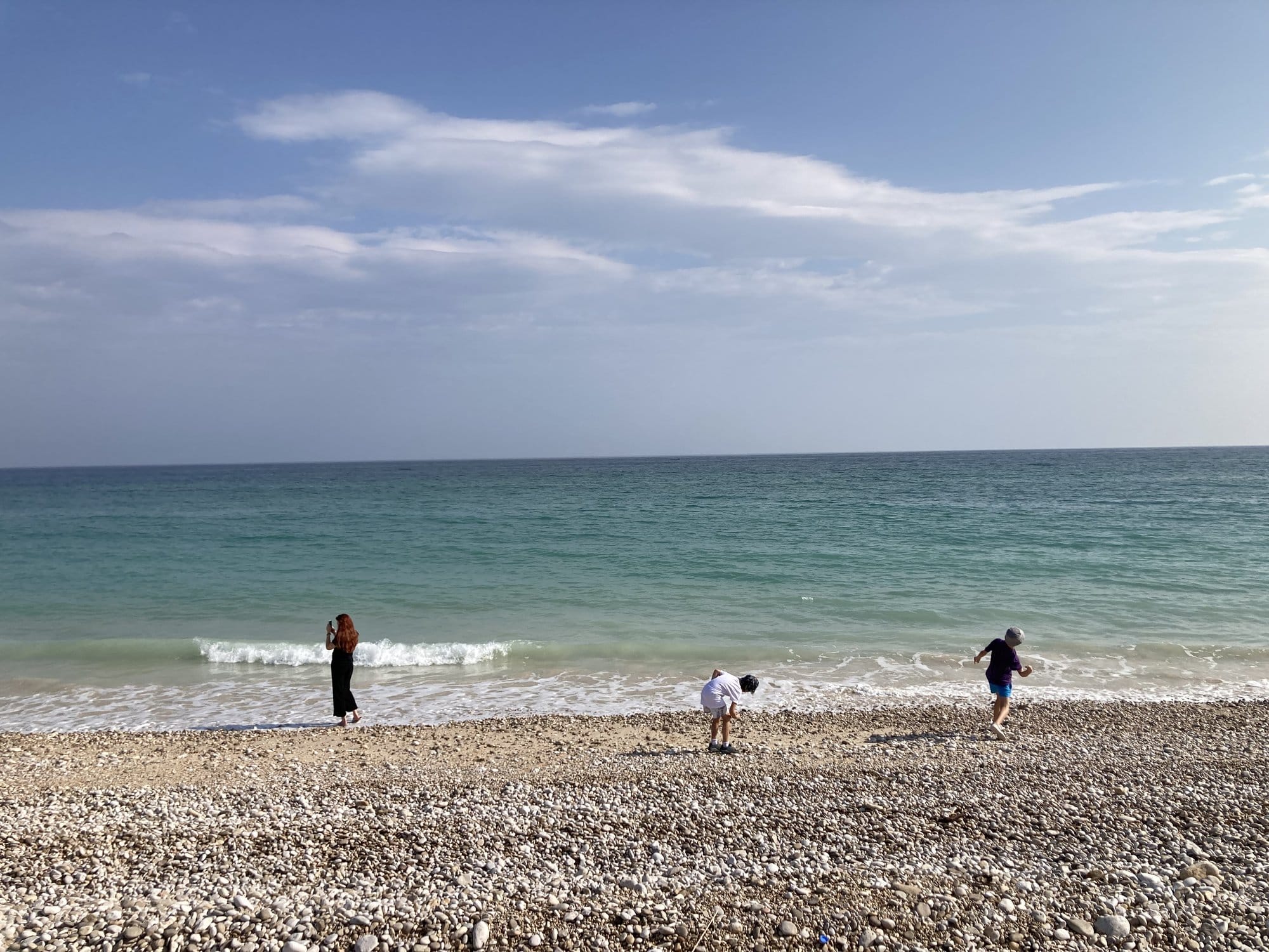 Family playing in the waves on a pebble beach with turquoise sea — Sur, Oman