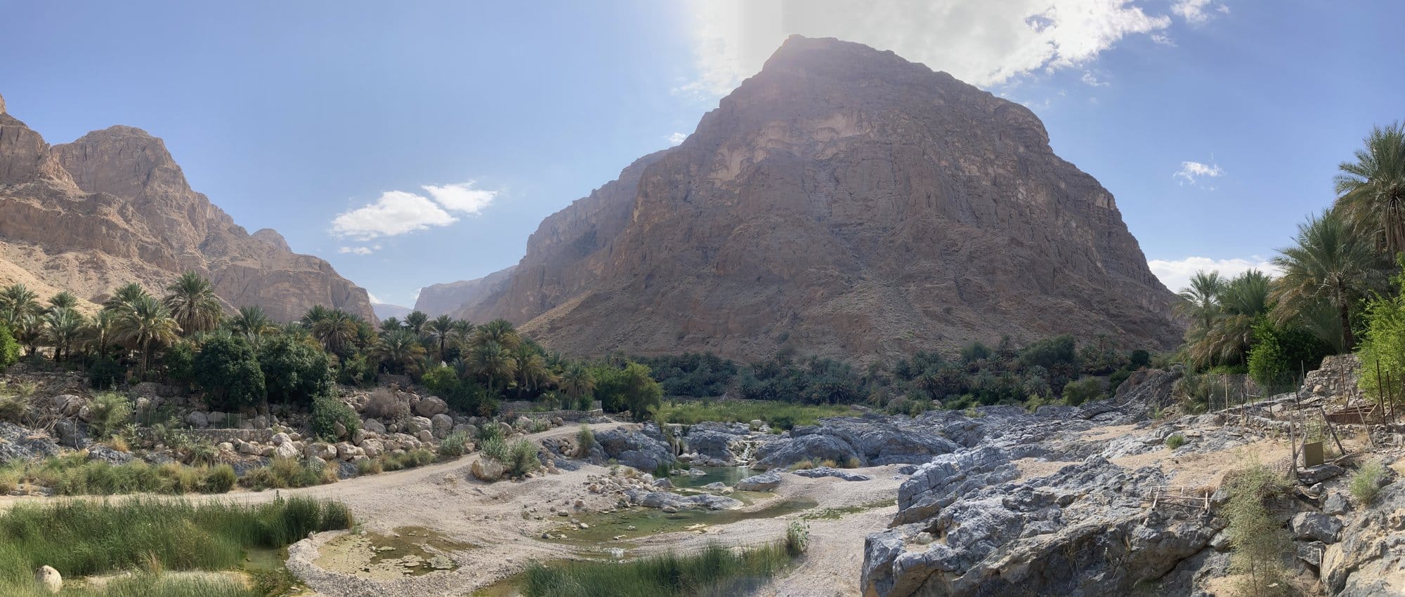 Panoramic view of a mountain valley with palm trees and a dry riverbed — Al Qābil, Oman