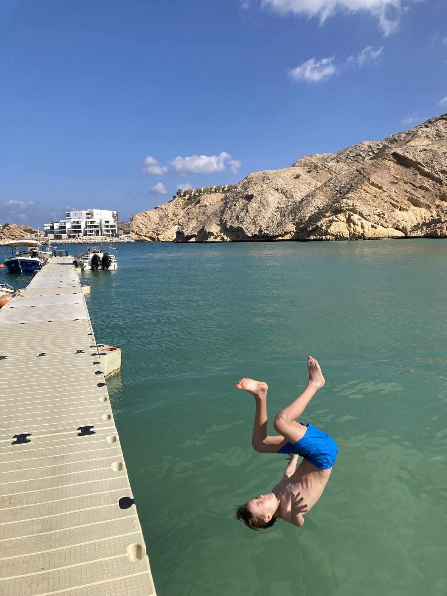 Child doing a backflip off a marina pontoon into turquoise water — Muscat, Oman