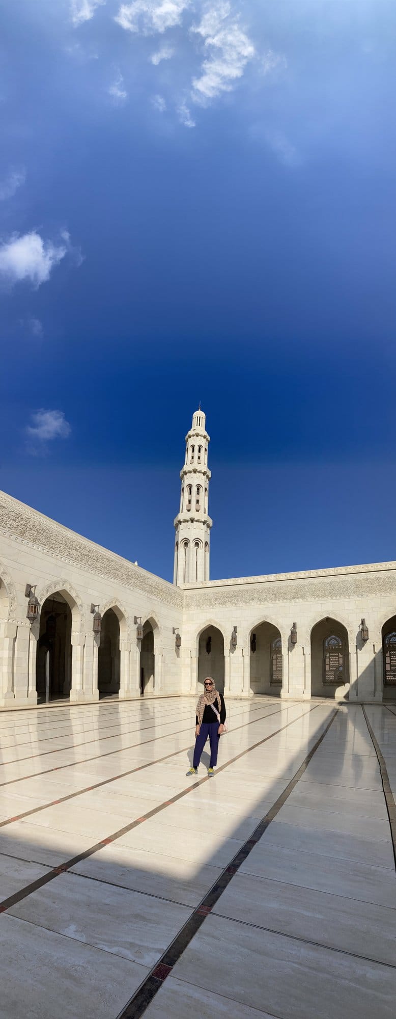 A lone figure in the vast white marble courtyard of the Sultan Qaboos Grand Mosque, minaret soaring above — Bawshar, Oman