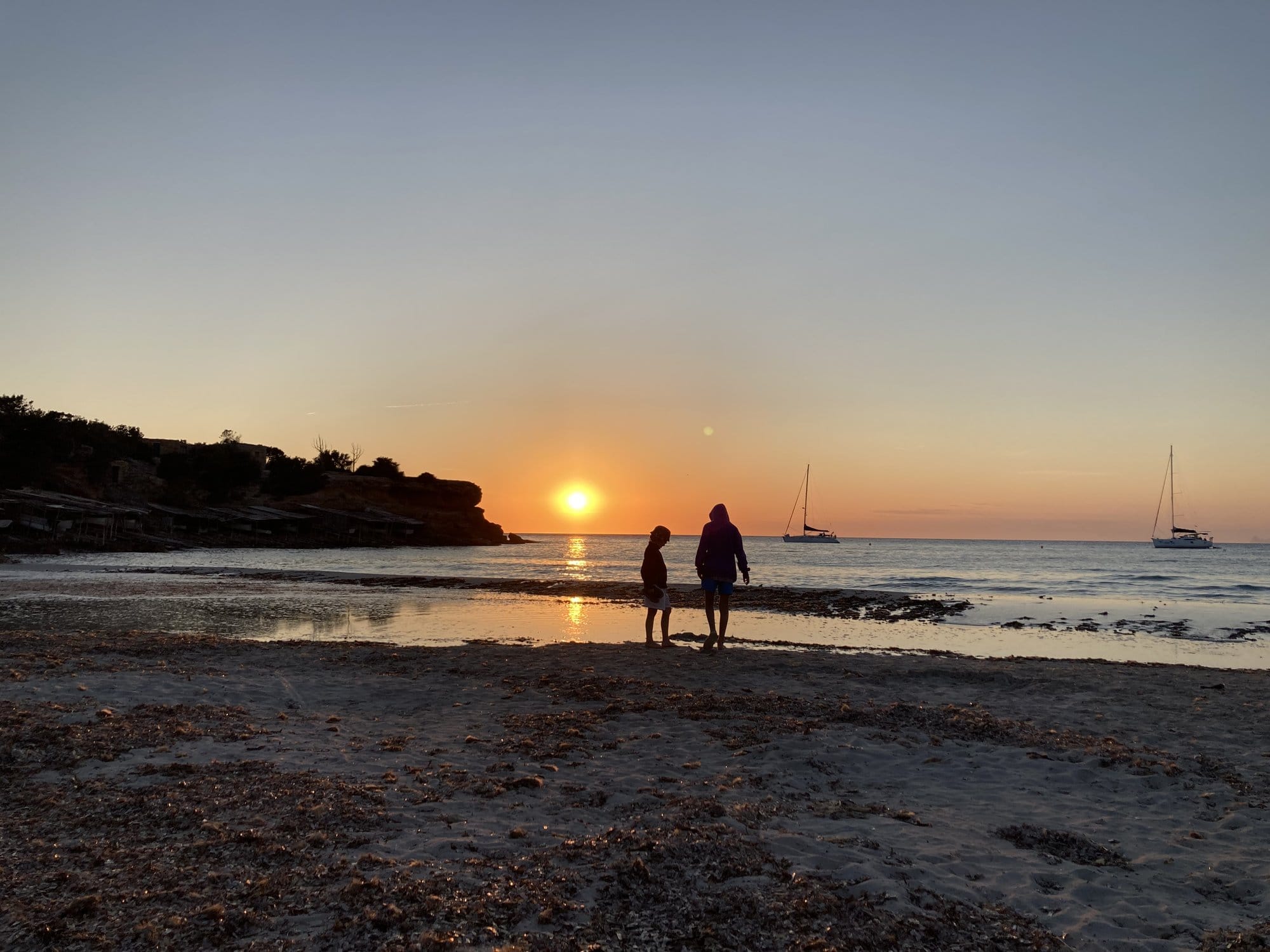 Two figures in shallow water at golden sunset — Formentera, Spain