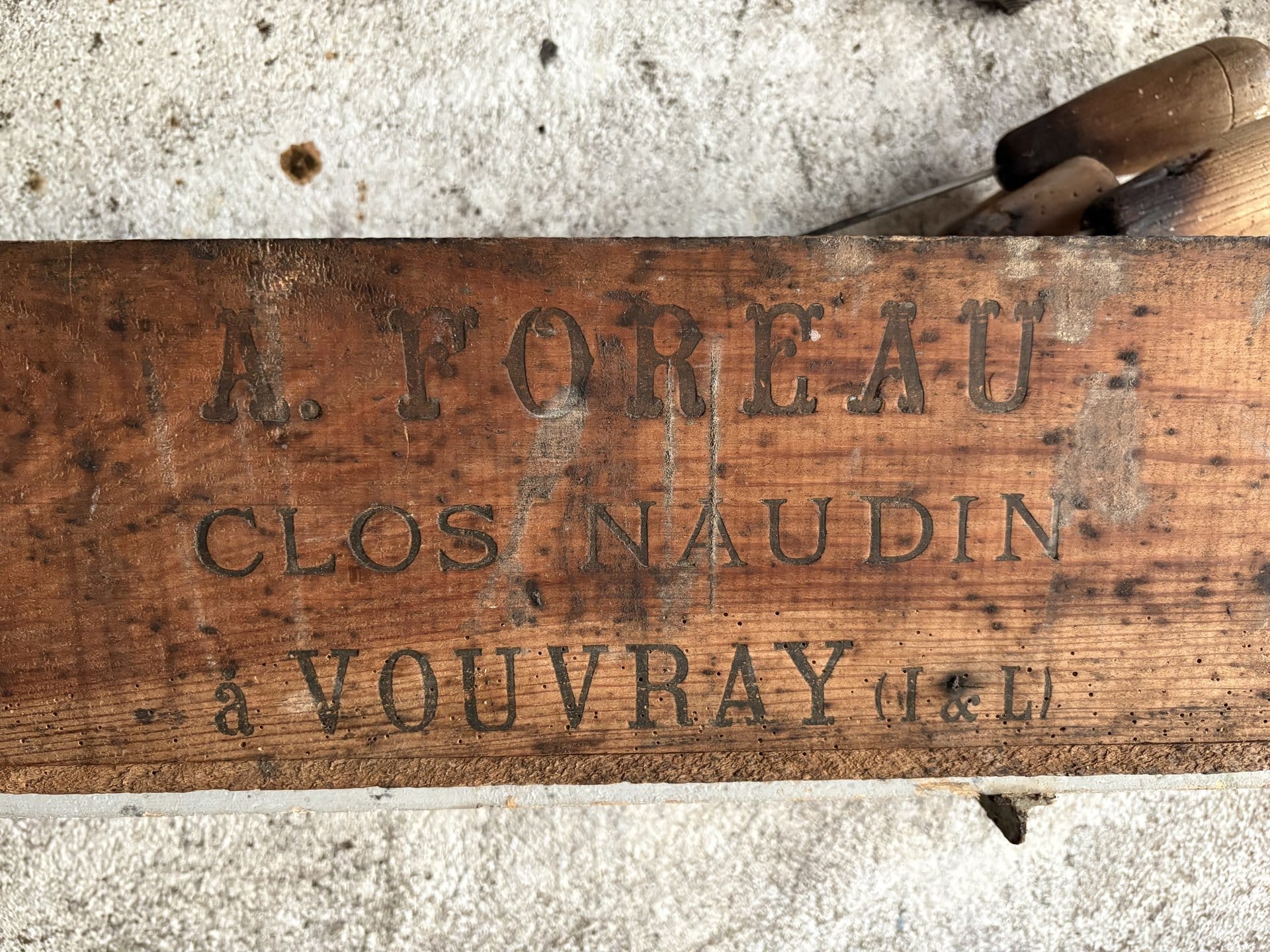 A wooden crate stencilled "A. FOREAU / CLOS NAUDIN / à VOUVRAY (I.&L.)" with old cooper's tools in the background — heritage at the Domaine du Clos Naudin