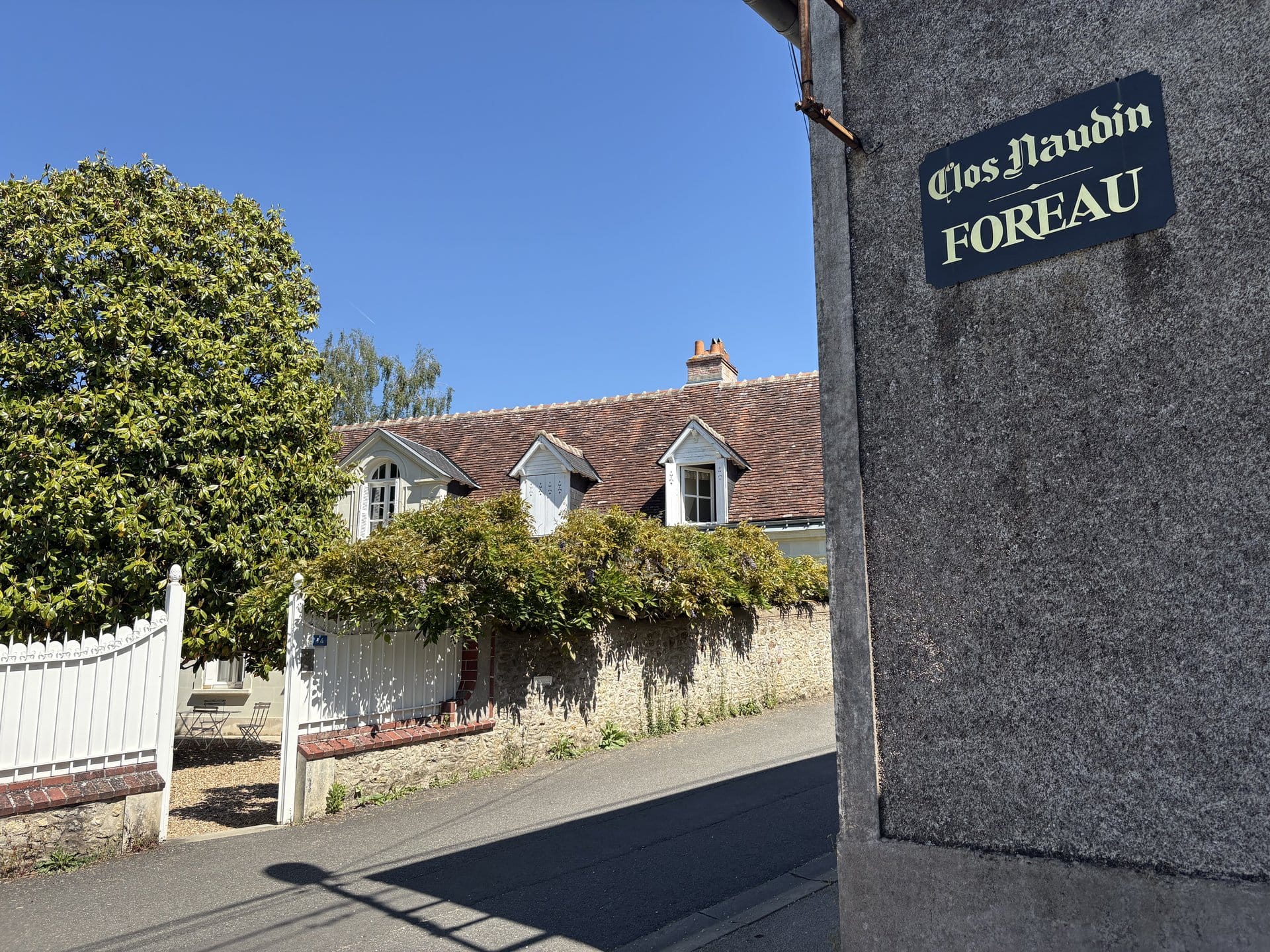 The pale-stone entrance of the Clos Naudin with a wisteria-covered wall and a blue enamelled "Clos Naudin / FOREAU" sign — Vouvray, Loire Valley
