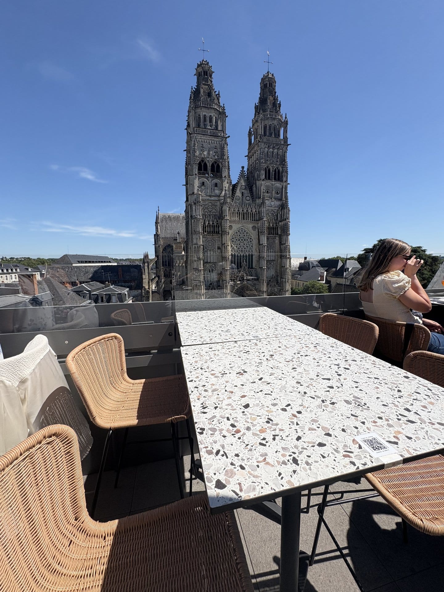 A terrazzo table on the rooftop terrace of La Belle Vue, with rattan chairs and the two flamboyant Gothic towers of the Cathédrale Saint-Gatien rising in the background — Tours