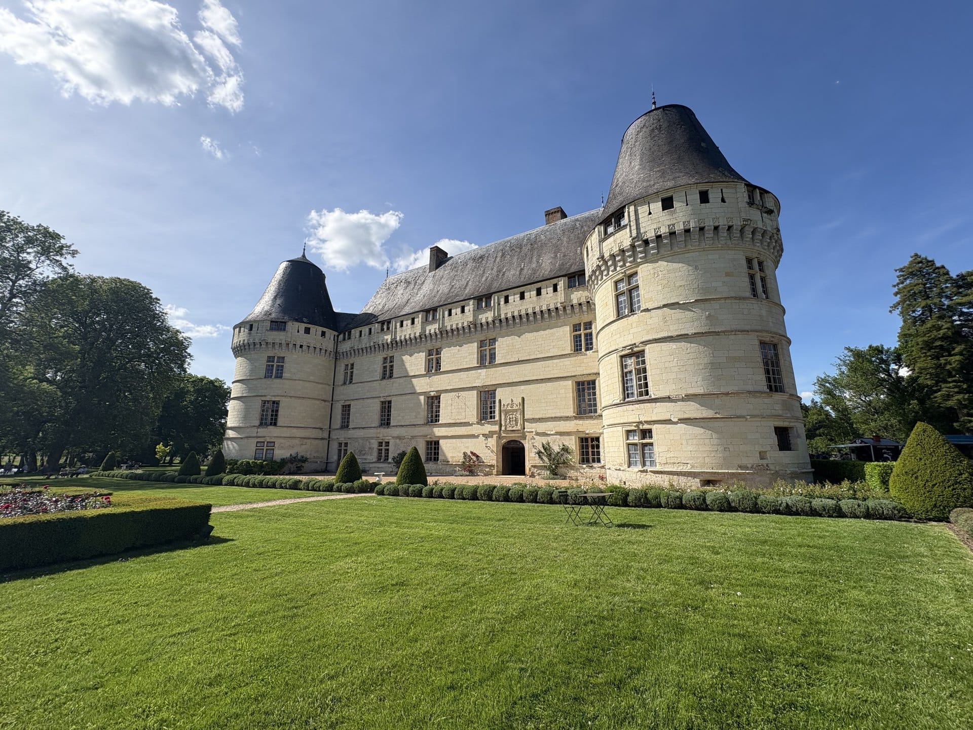 The pale tuffeau façade of the Château de l'Islette seen from its garden, two round towers with conical slate roofs, a flowerbed and gravel path in the foreground — Cheillé, Loire Valley