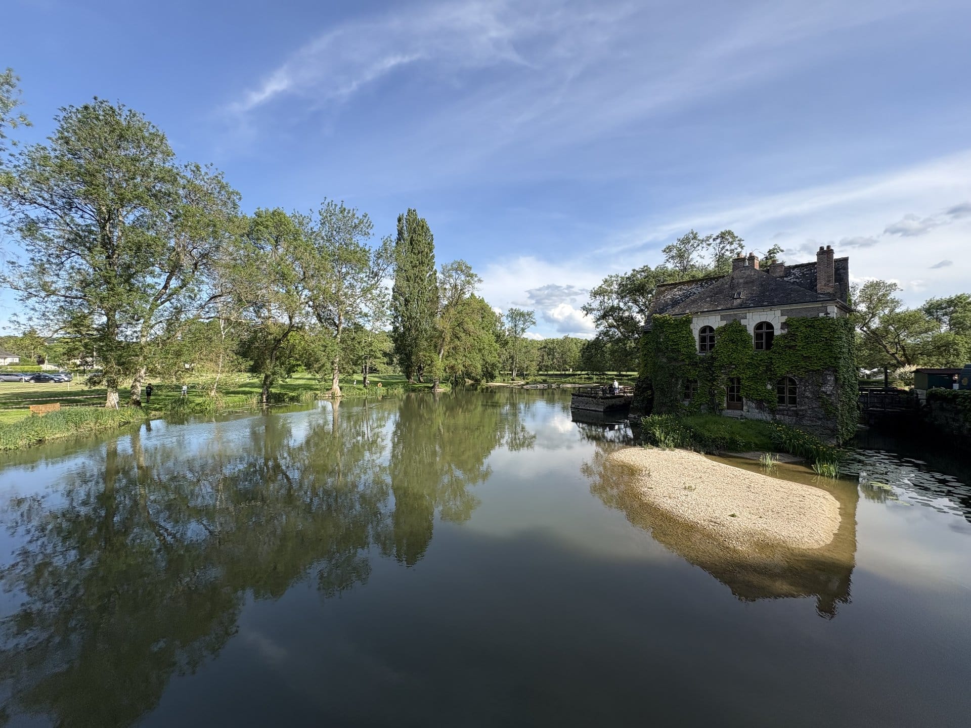 View from the bridge over the Indre at the Château de l'Islette: a stone outbuilding covered in ivy, a small crenellated tower, sandbank below and golden late-afternoon reflections on the water