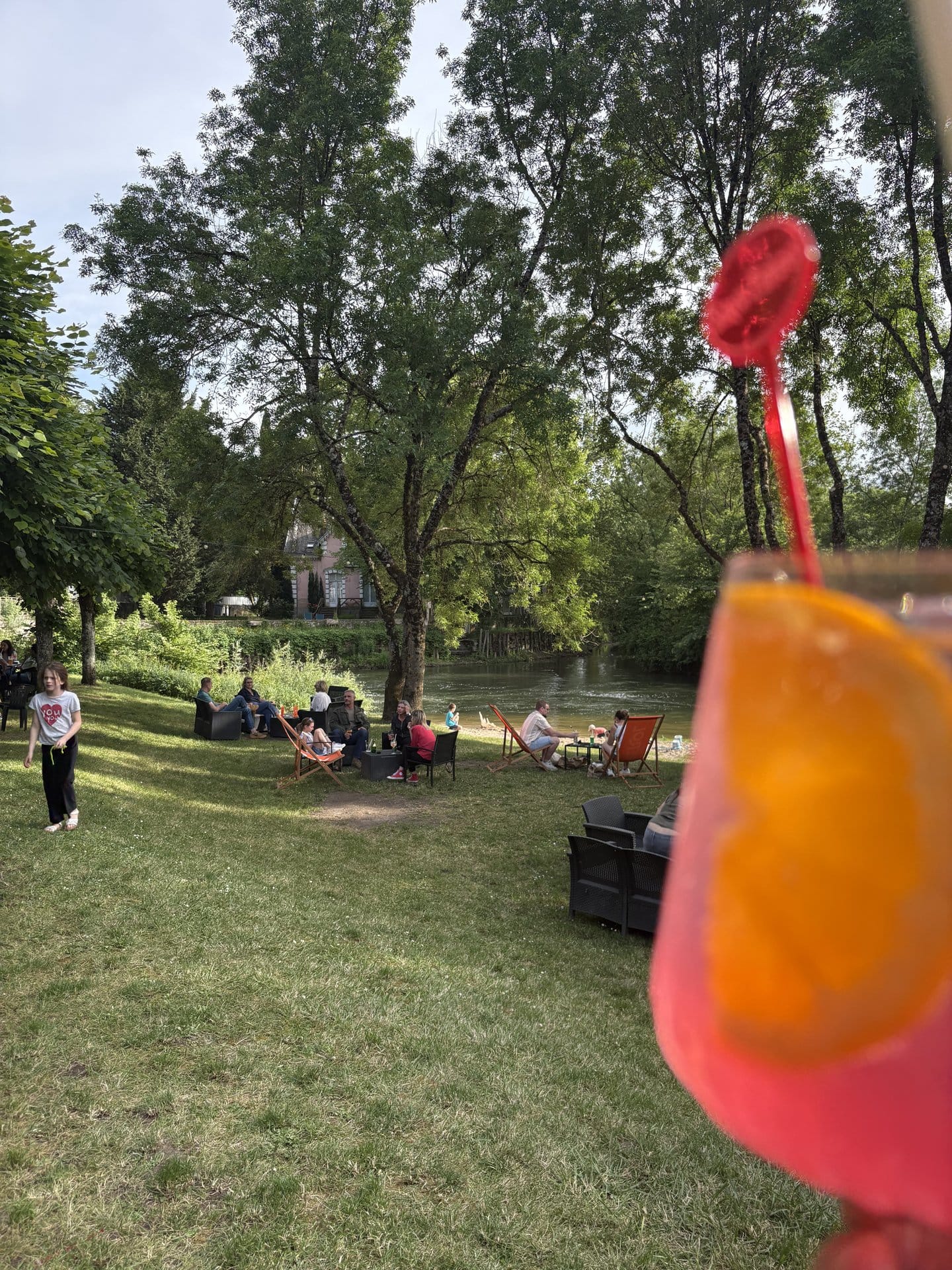 A bright orange popsicle ice cream half-eaten on a wooden picnic table at L'Îlot d'Azay, lawn and other guests in soft focus behind