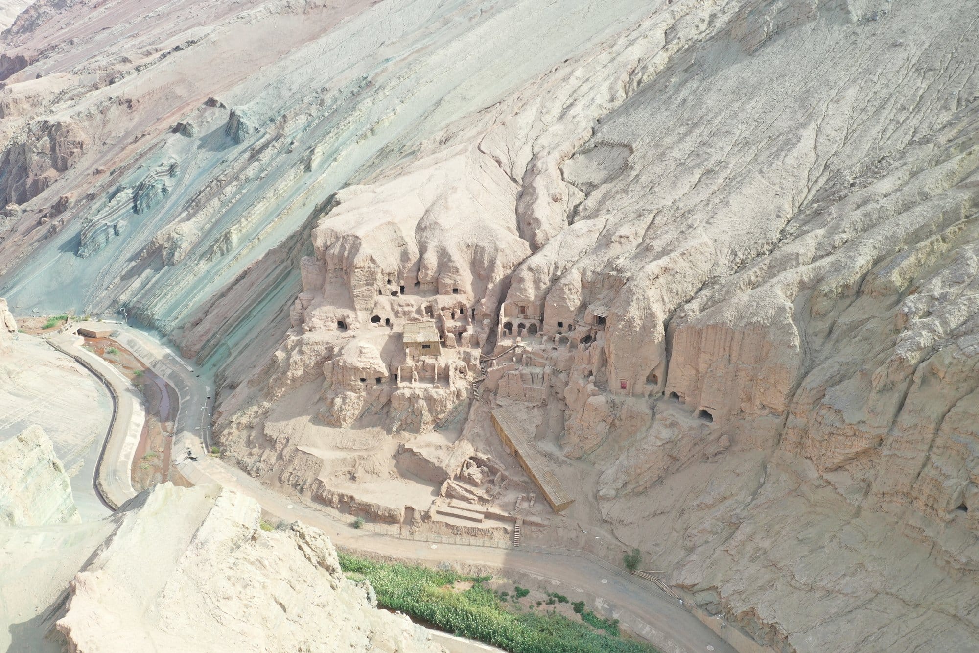 Cave dwellings and buildings cut into a pale cliff, the road and a band of green below. Shot with a DJI Mavic 2 Pro.