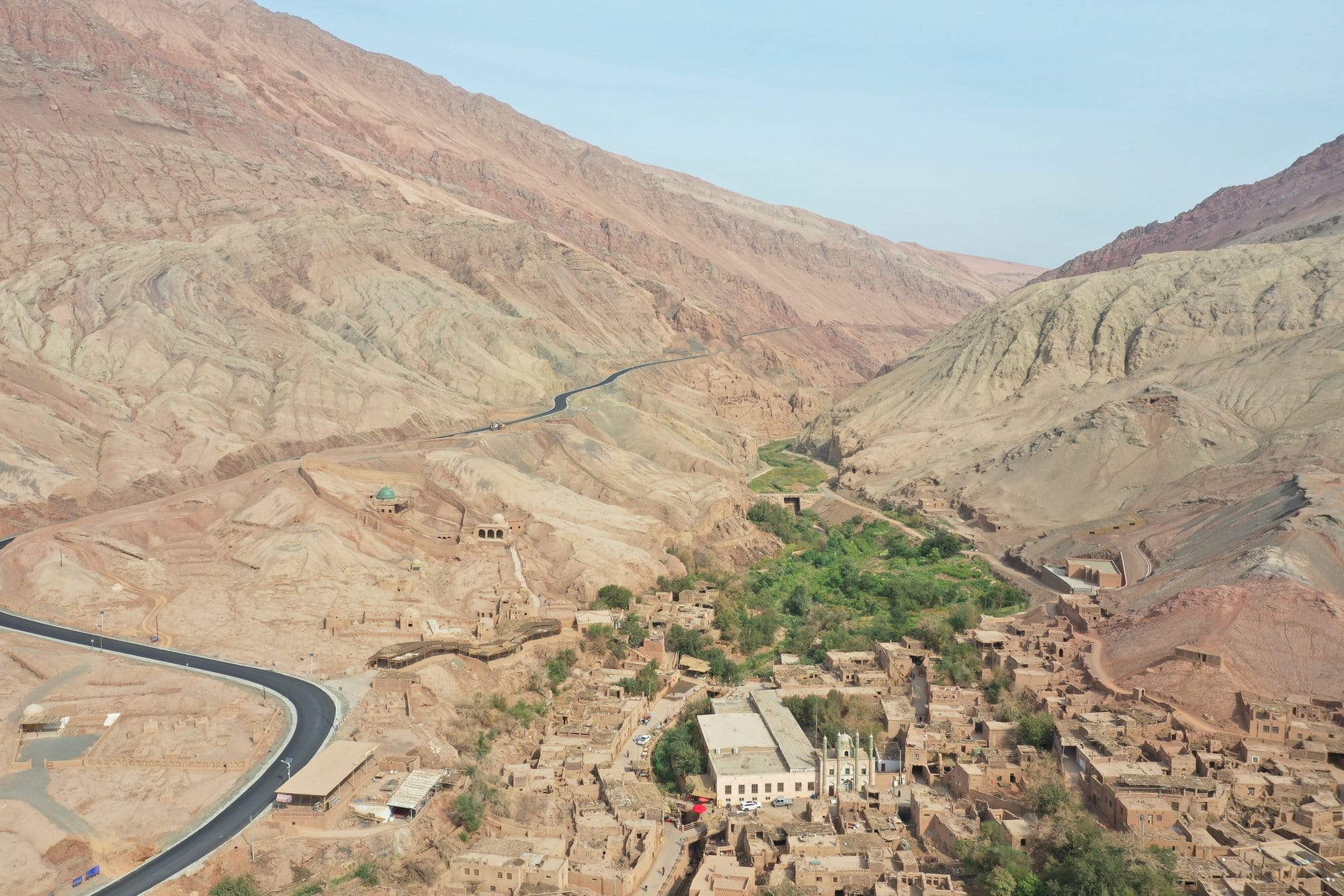 Looking down on the village at the bottom of its valley, the road winding between the earth houses and a stand of trees. Shot with a DJI Mavic 2 Pro.