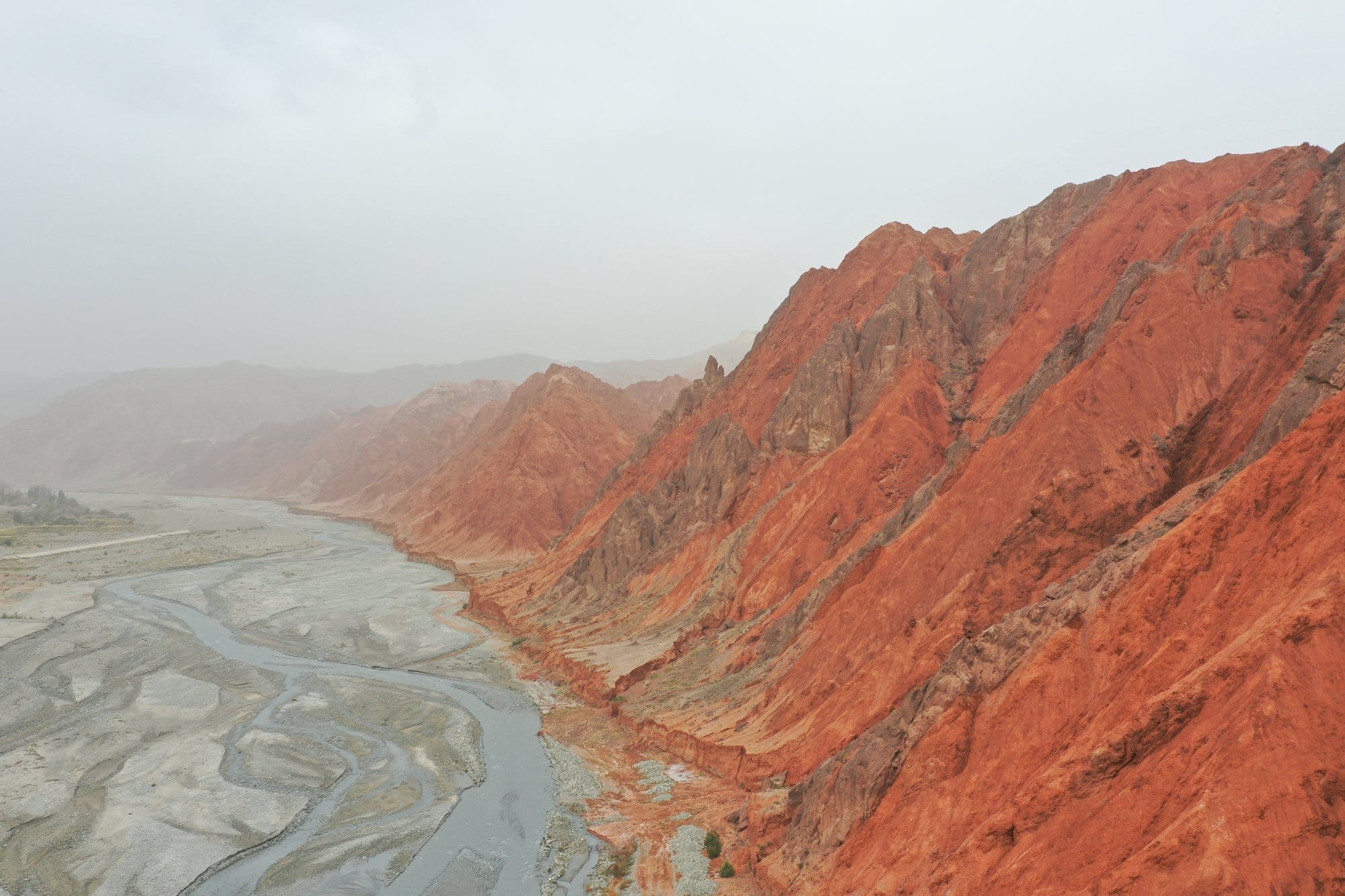 Red sandstone cliffs above the grey braided river at Ghez, haze filling the far end of the canyon. Shot with a DJI Mavic 2 Pro.