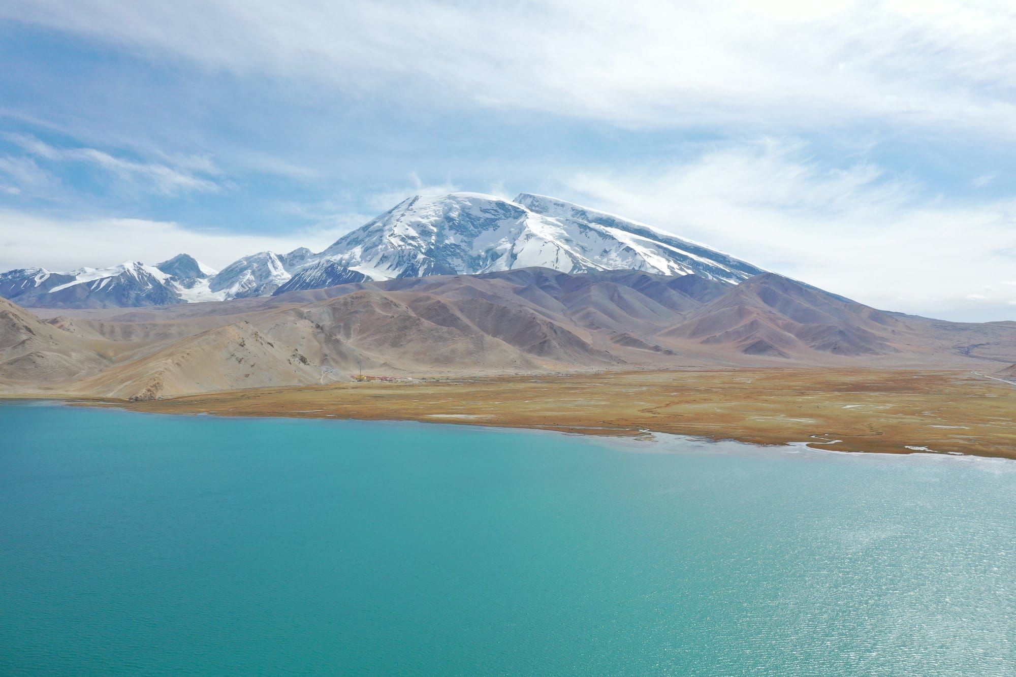 Turquoise water, ochre grass and the snow mass of Muztagh Ata under high cirrus. Shot with a DJI Mavic 2 Pro.