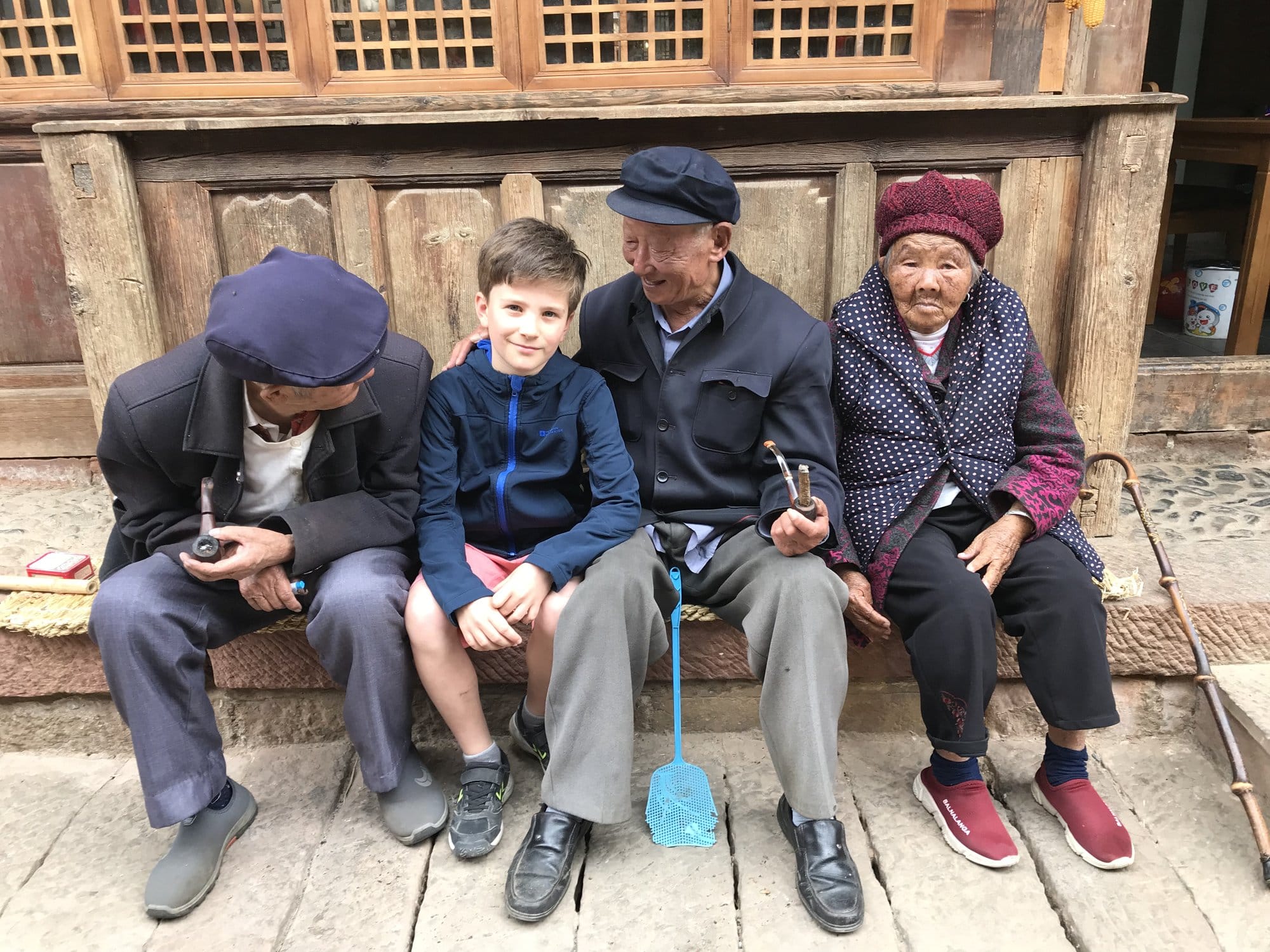 Three village elders on a stone bench, making room for a visiting child.