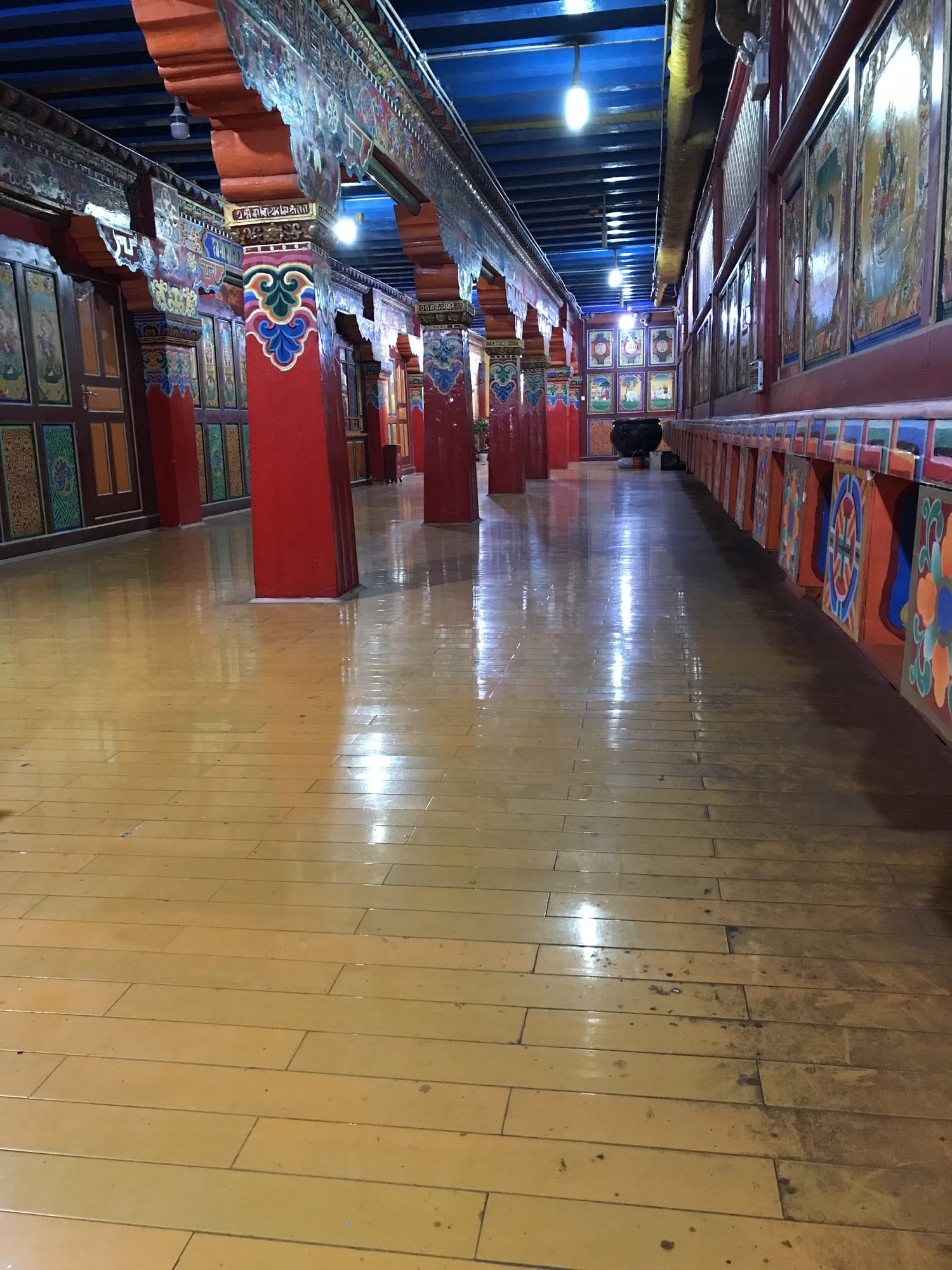 The interior gallery of the monastery, red painted columns and thangkas along the wall.