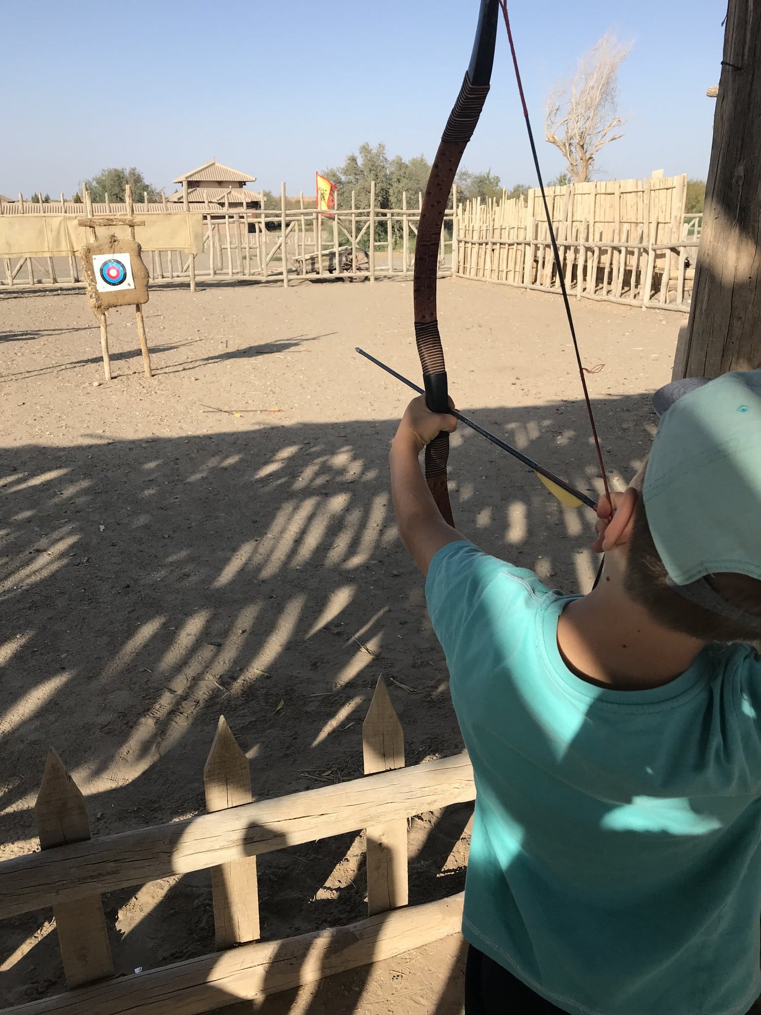 A child shooting at a target inside the reconstructed frontier post at Yangguan, a watchtower behind the palisade.