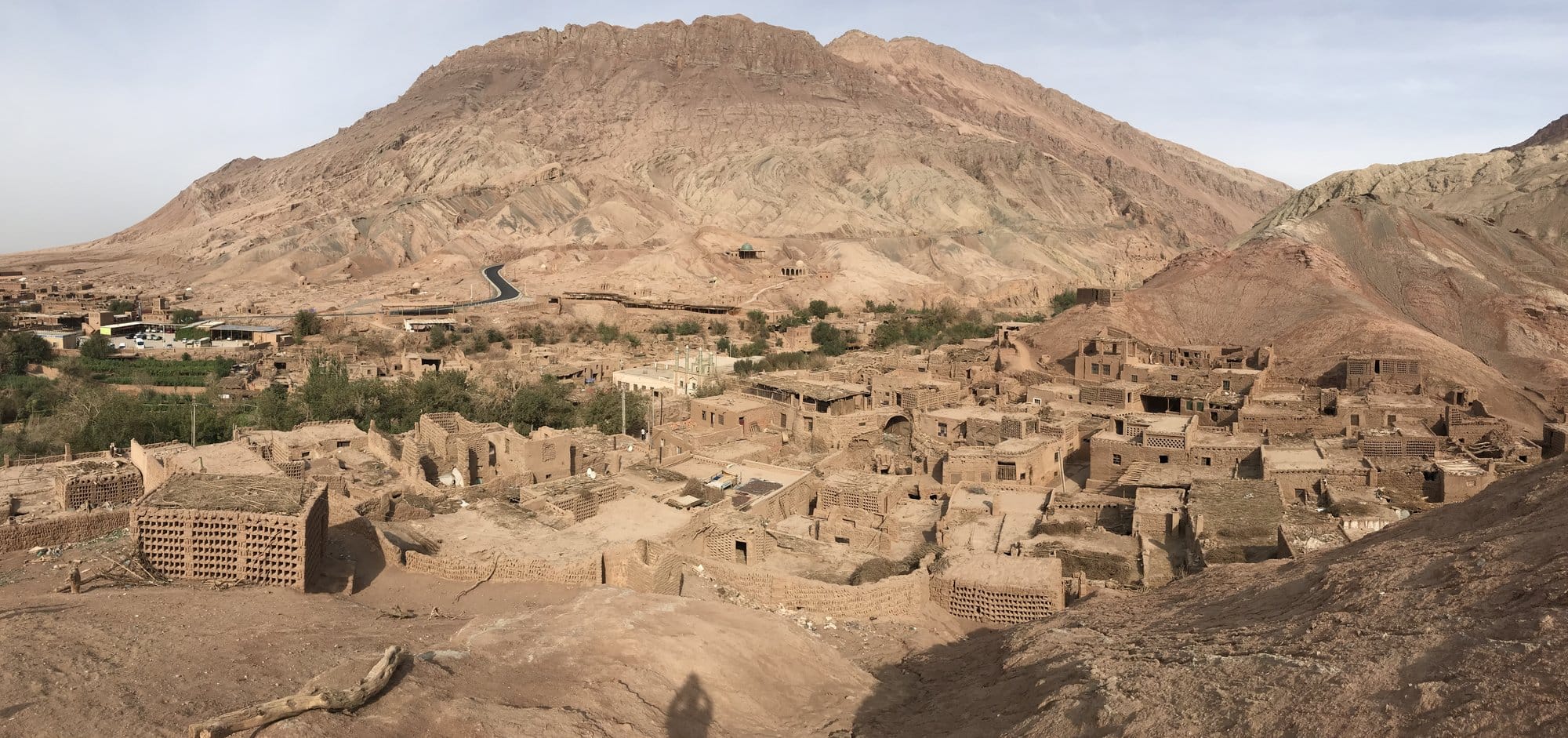 The village of Tuyoq in mud brick at the foot of an arid mountain, the road curling down towards it.