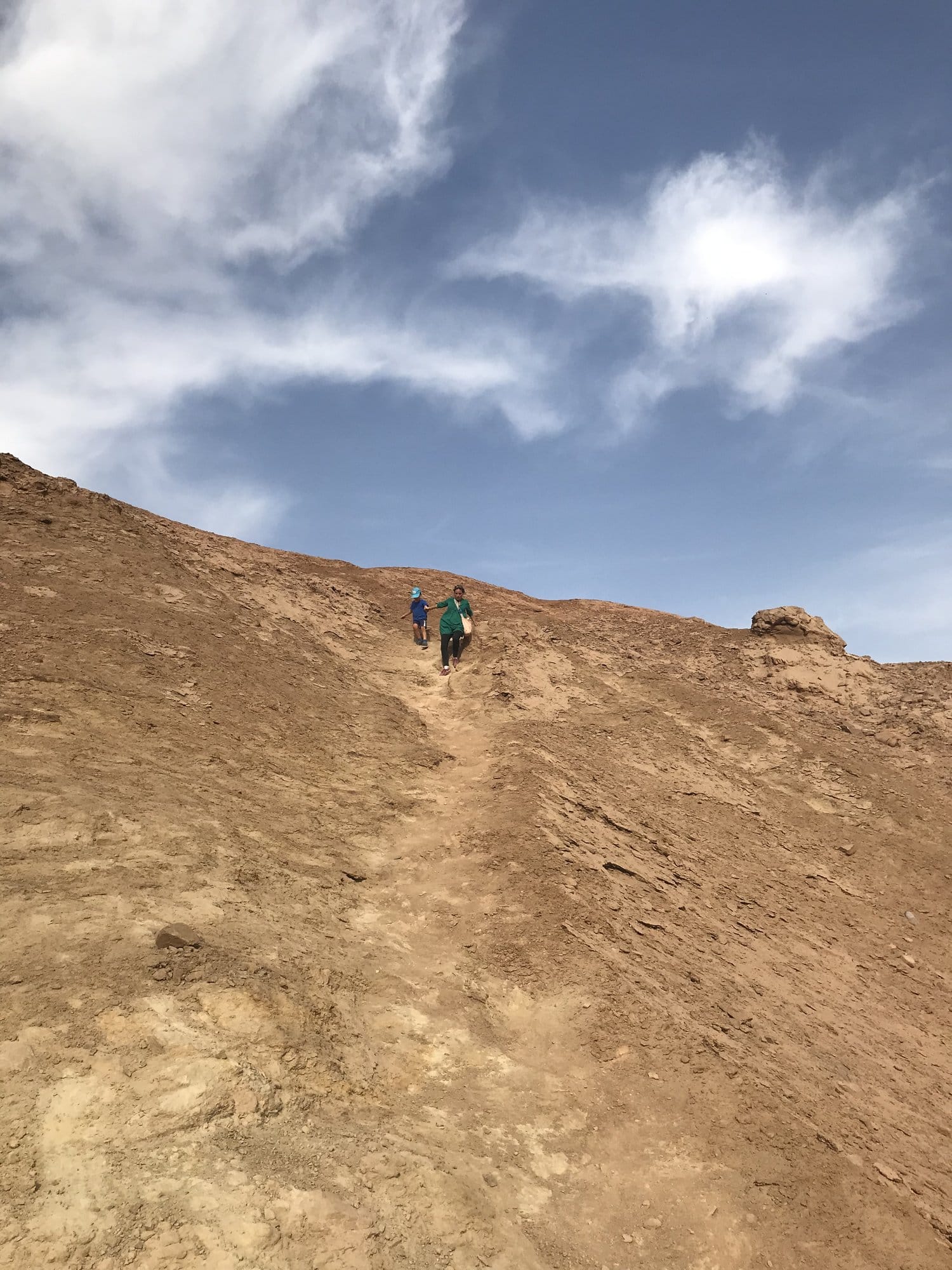 Two of us coming down a path on an ochre slope under a wide blue sky.
