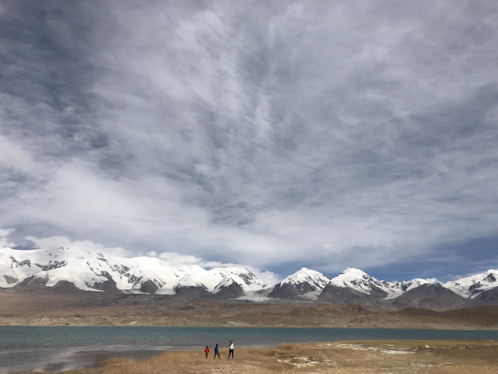 A line of snow peaks behind the lake under an enormous streaked sky.