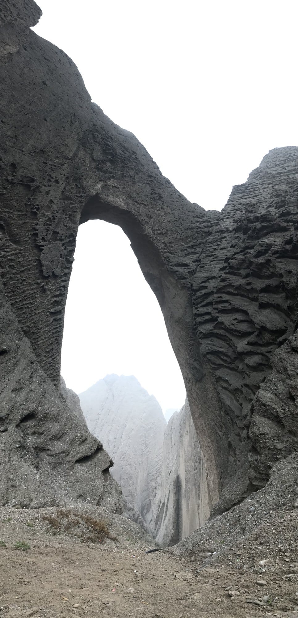 Shipton's Arch from below: a vault of grey conglomerate opening onto a corridor of mist.
