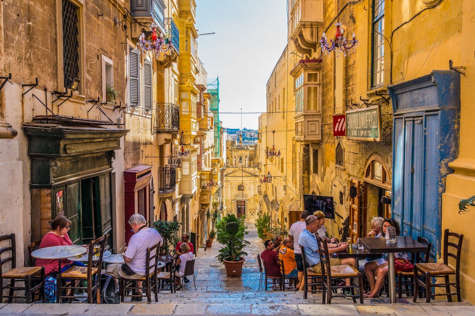 Mesas de café en una calle empinada de La Valeta, Malta, entre casas con balcones de madera