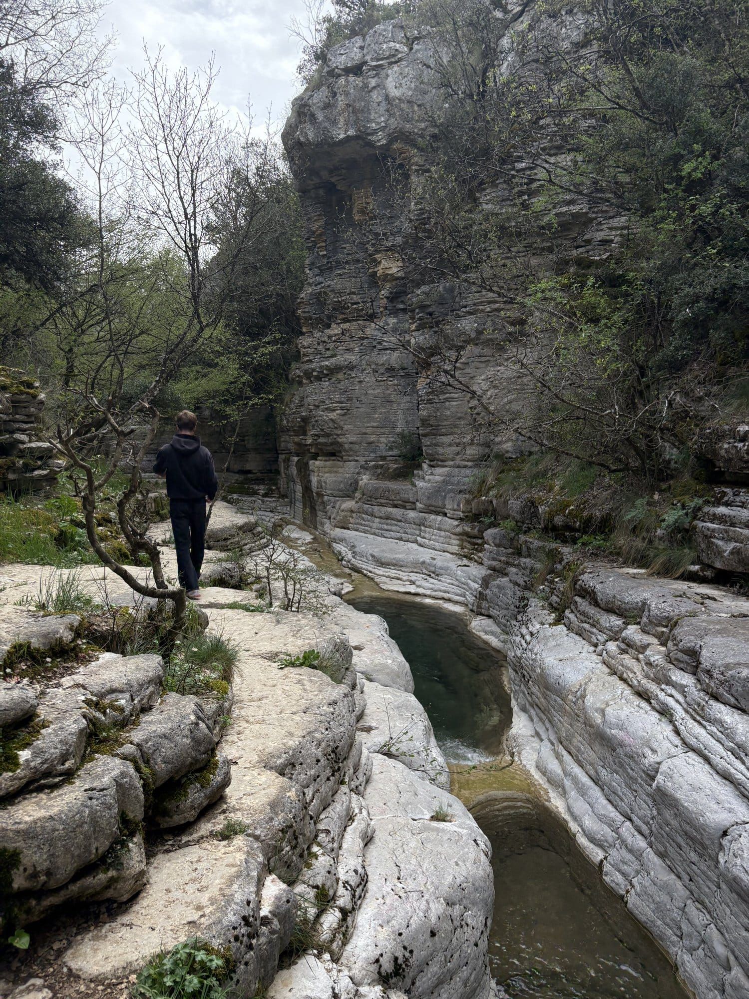 Un randonneur marque une pause au-dessus de l'une des vasques aux eaux vertes de Papingo (Kolymbithres) — Zagori, Grèce