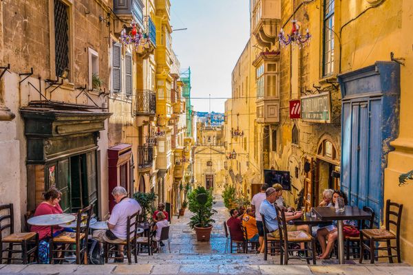 Mesas de café em uma rua íngreme de Valletta, em Malta, entre casas com varandas de madeira