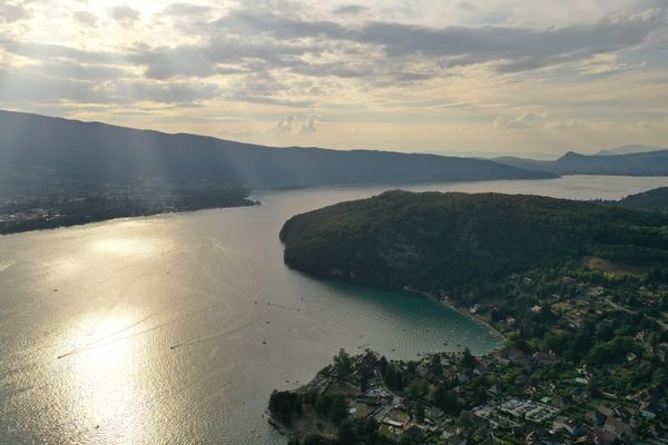 Aerial view of Lac d'Annecy at golden hour, with the wooded peninsula of Duingt in silhouette and the Tournette massif in the background