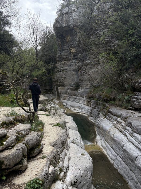 A walker pauses above one of the green-water Rock Pools of Papingo (Kolymbithres) — Zagori, Greece