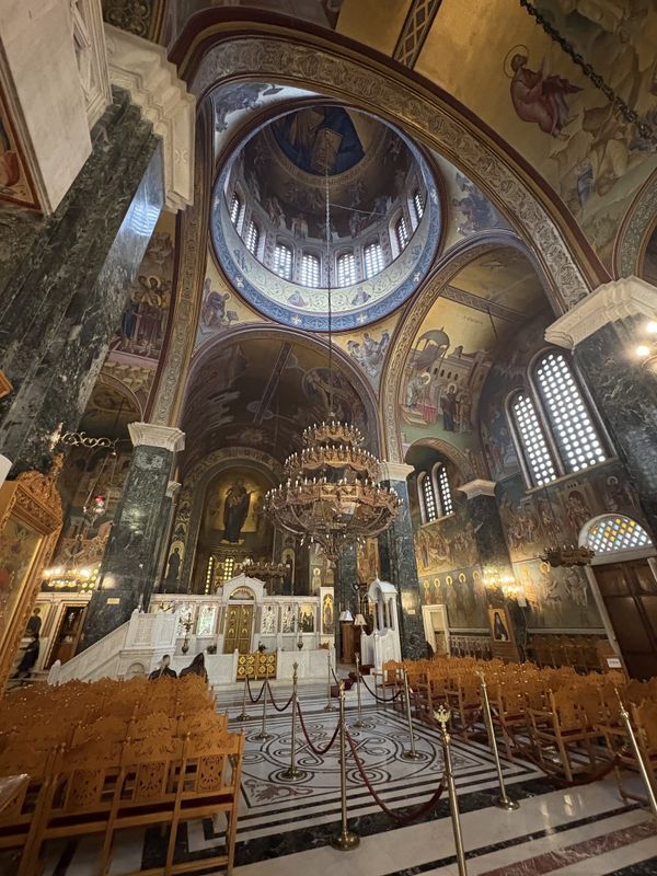 Interior of an Orthodox church in Thessaloniki with painted dome, chandeliers, frescoes and green marble columns — Greece