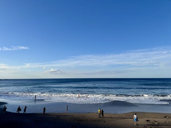 Playa de Benijo at golden hour, with surfers in the water, a black-sand beach, and two iconic sea stacks rising offshore — Tenerife