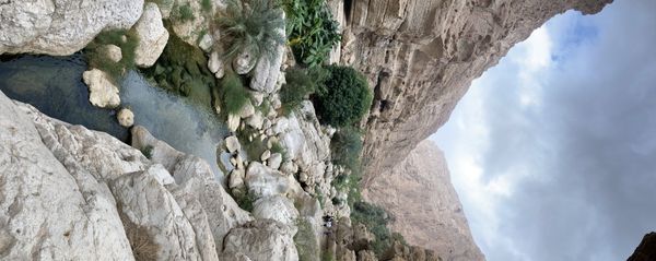 Wadi Shab canyon pool under a massive limestone overhang, palms clinging to the walls, turquoise water, no people