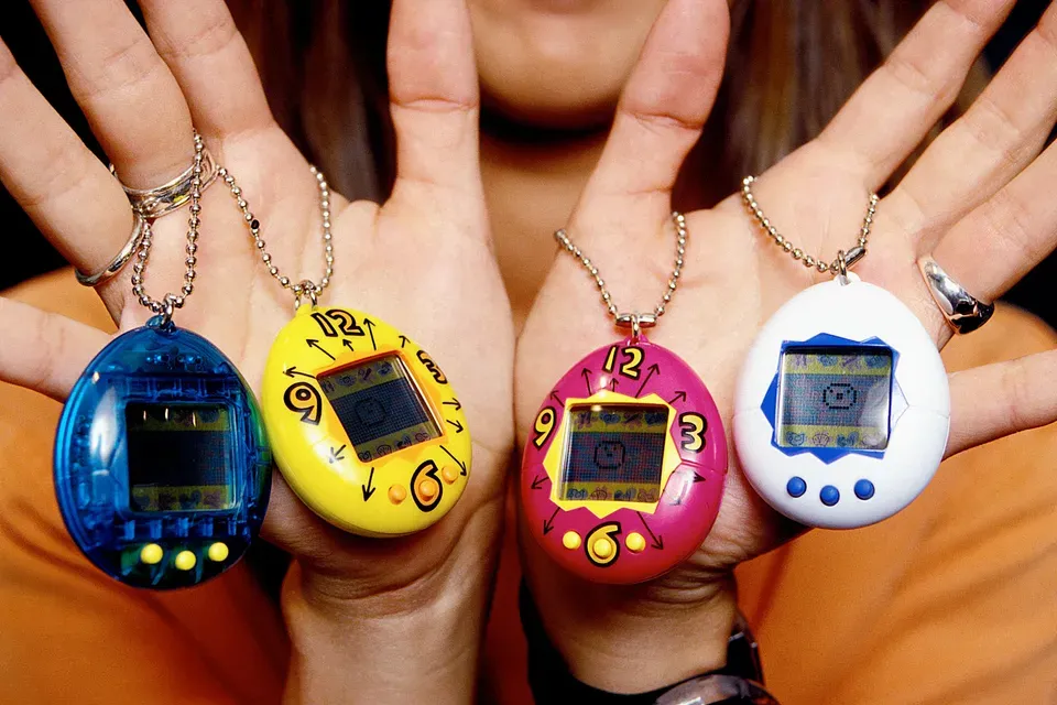 A set of caucasian hands holds 4 Tamigotchi toys.